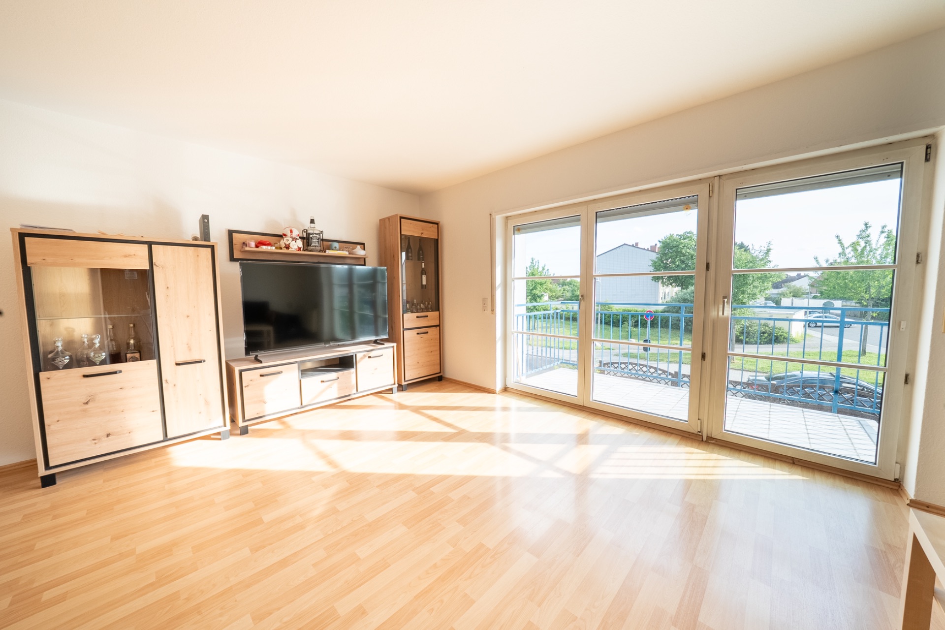 Helles Wohnzimmer mit Holzfußboden, TV, Schränken und großen Fenstern zur Terrasse.