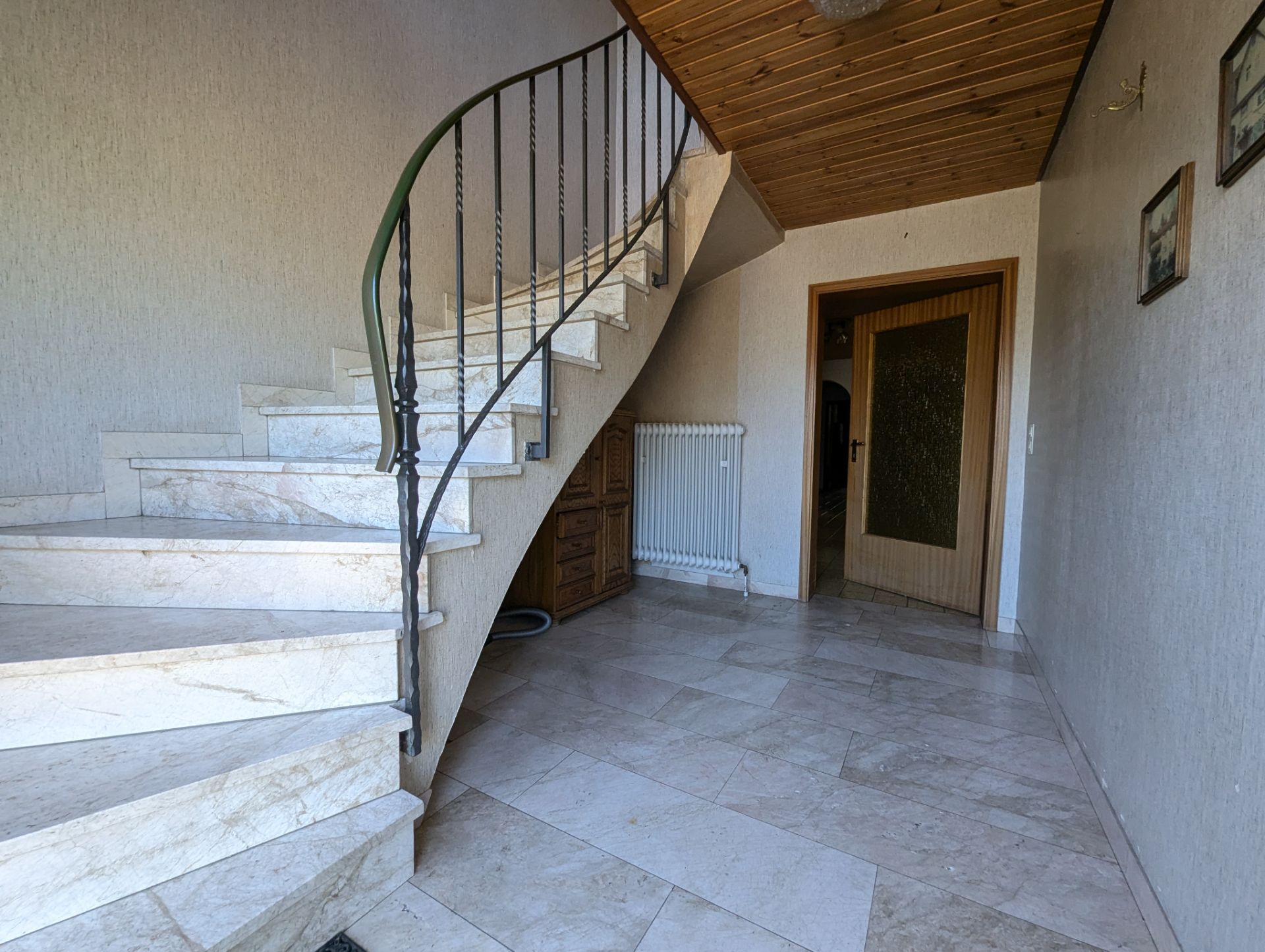 Heller Flur mit Marmortreppe und Holzdecke, Tür und Heizkörper sichtbar.