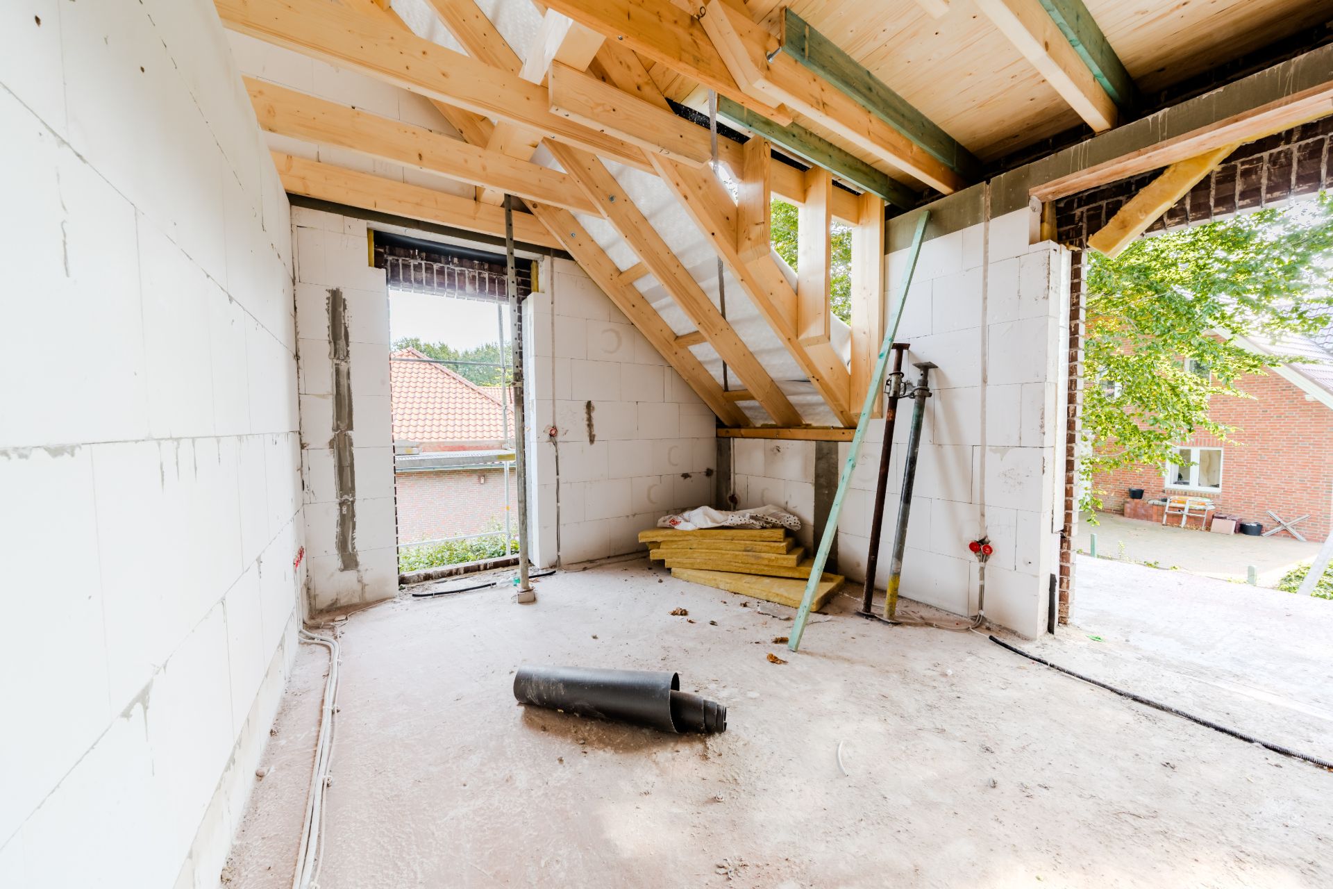 Heller Raum im Rohbau mit sichtbaren Holzbalken, Baumaterialien und offenen Durchgängen.