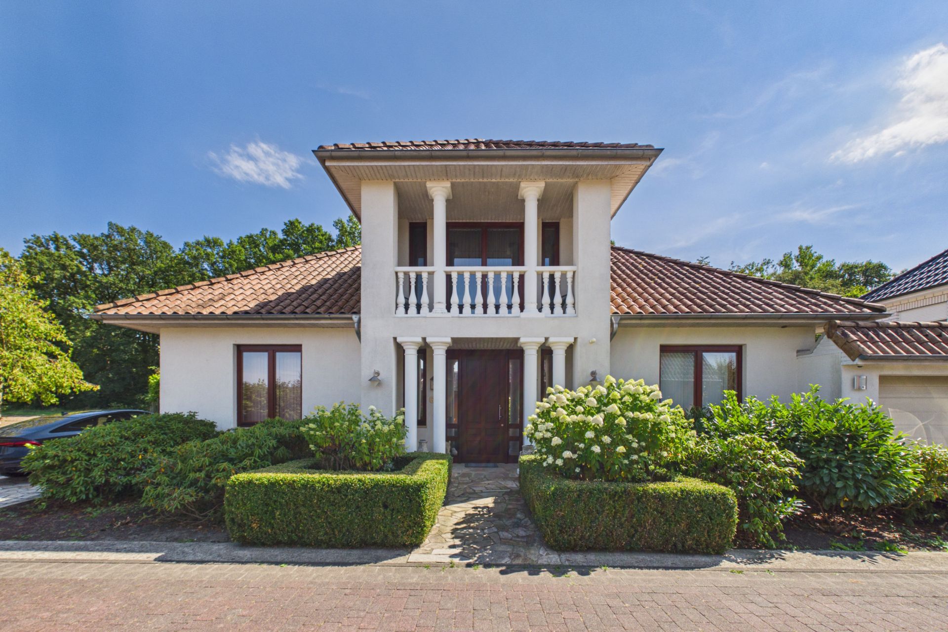 Modernes Einfamilienhaus mit Balkon, rotem Ziegeldach und gepflegtem Garten vor dem Eingang.