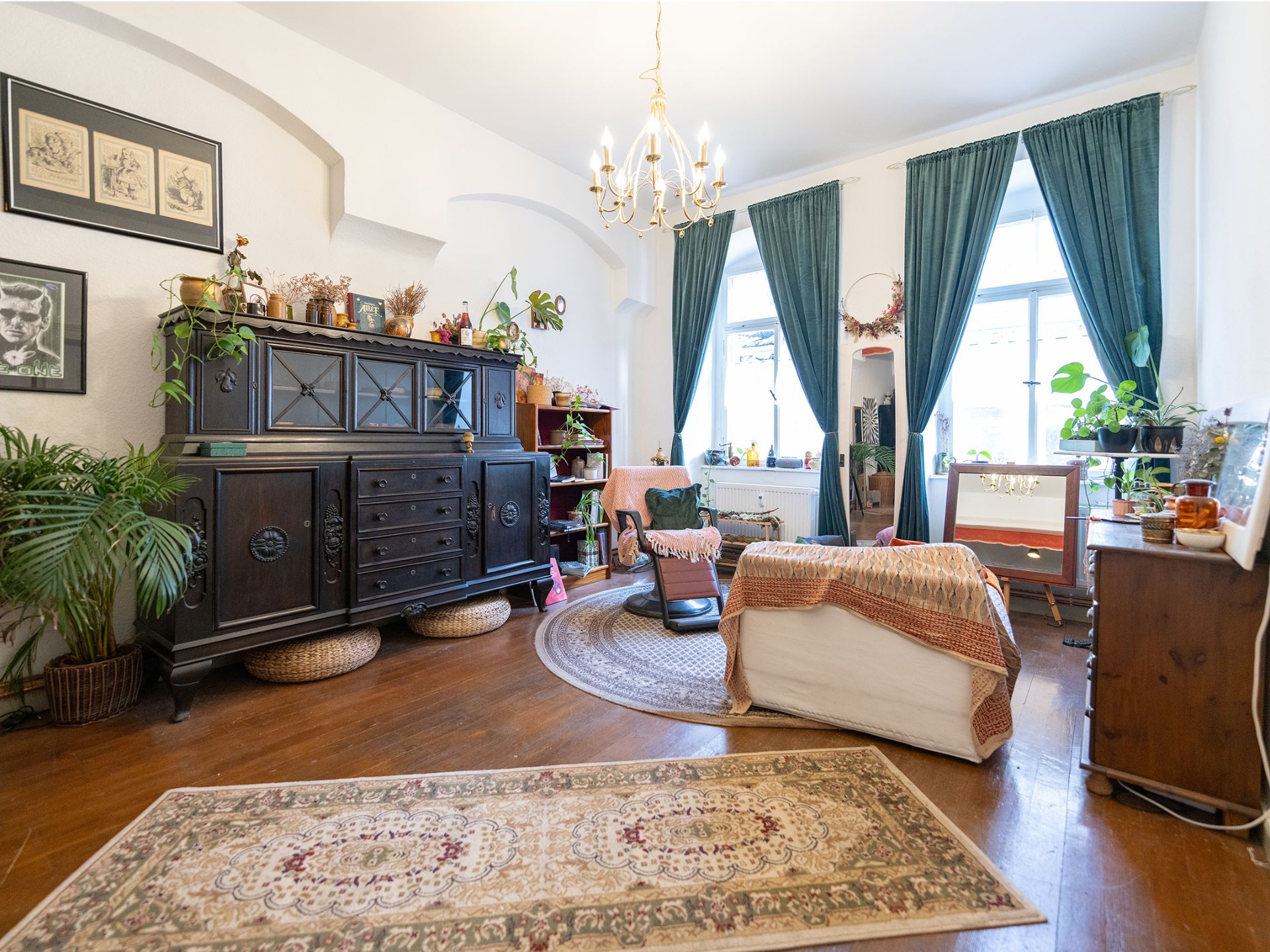 Helles Wohnzimmer mit Teppich, Vorhängen, Sessel, Sideboard und vielen Pflanzen.
