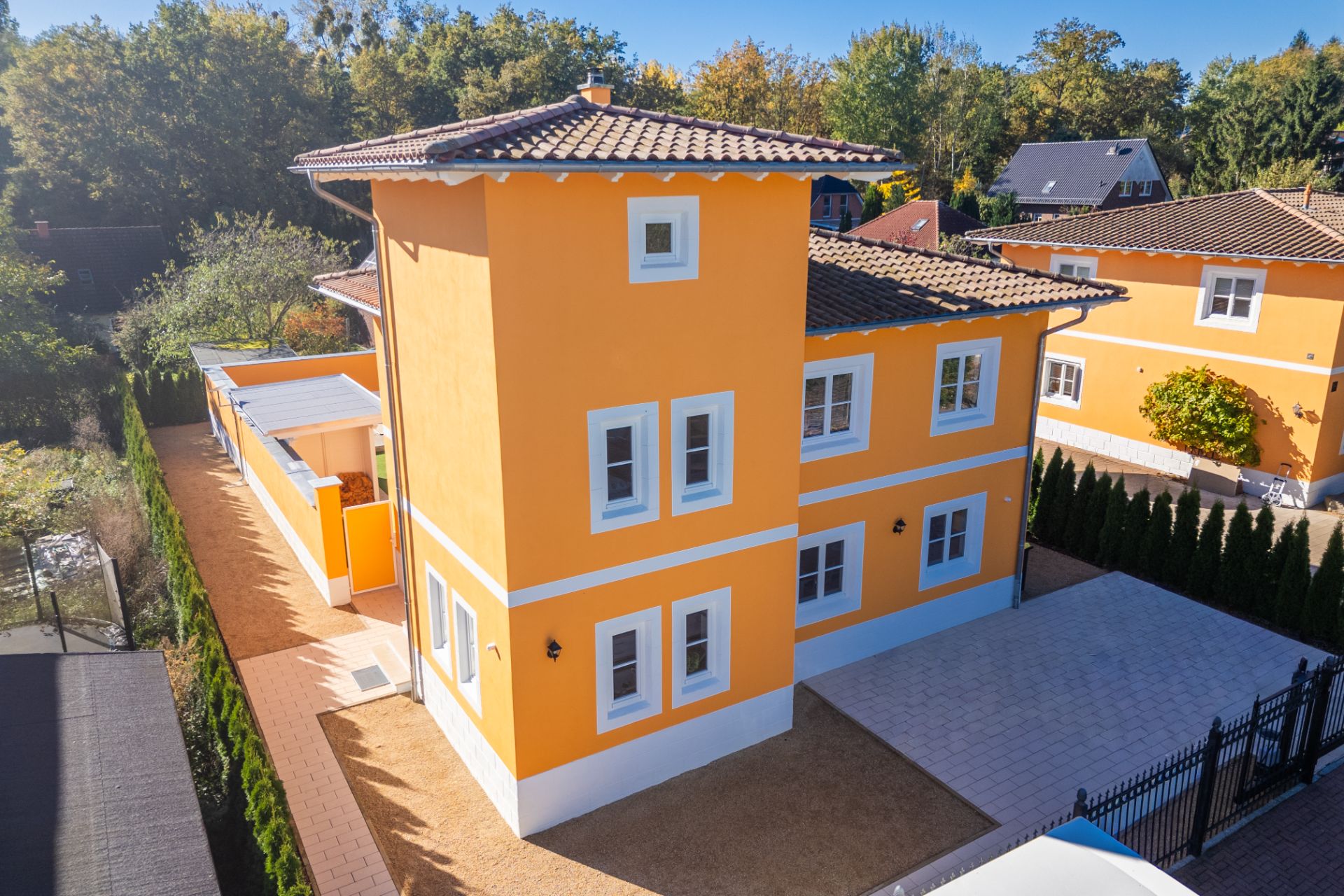 Modernes, orangefarbenes Wohnhaus mit weißem Rahmen und mehreren Fenstern, umgeben von Bäumen.