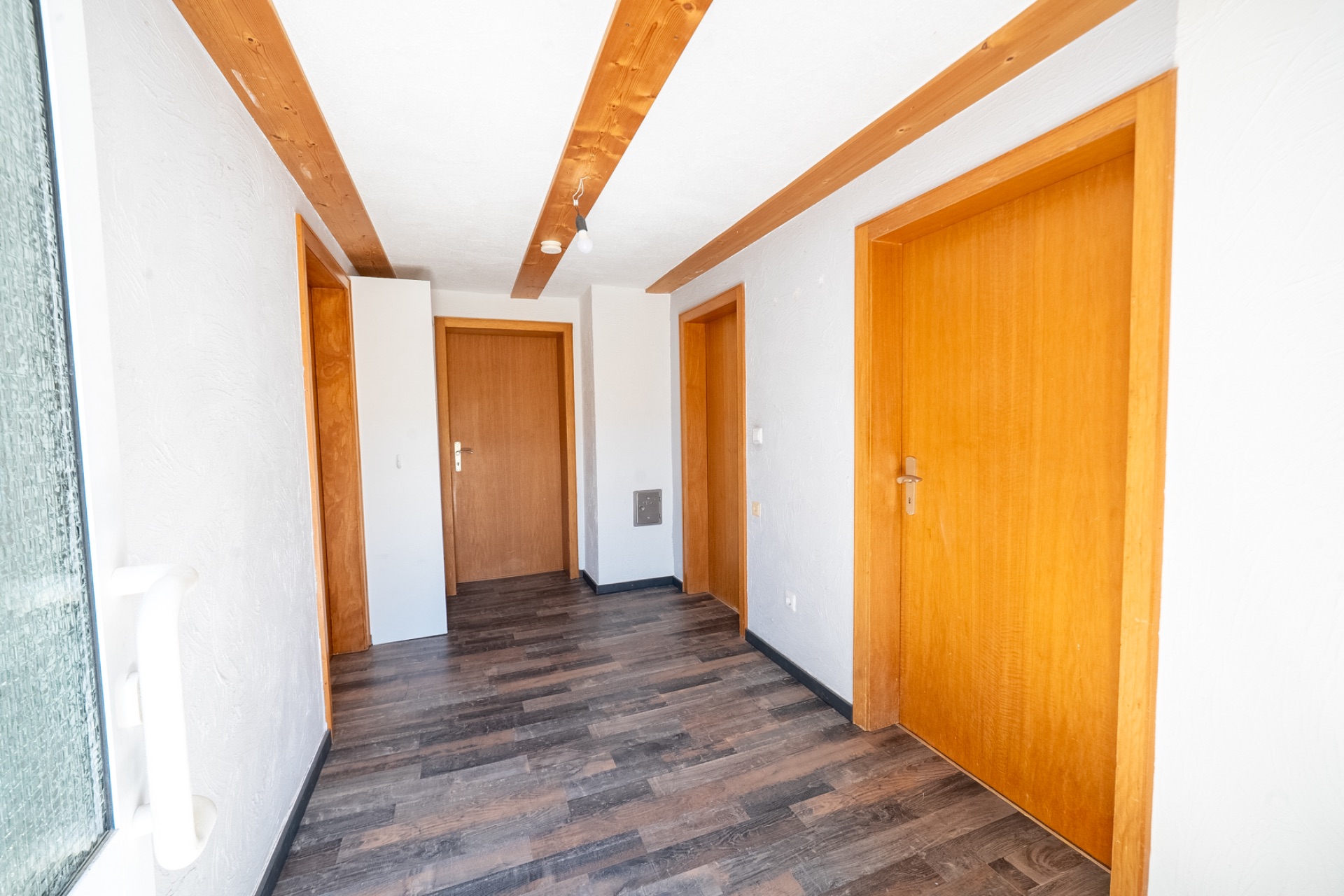 Heller Flur mit Holztüren und Holzbalken an der Decke, dunkler Boden.