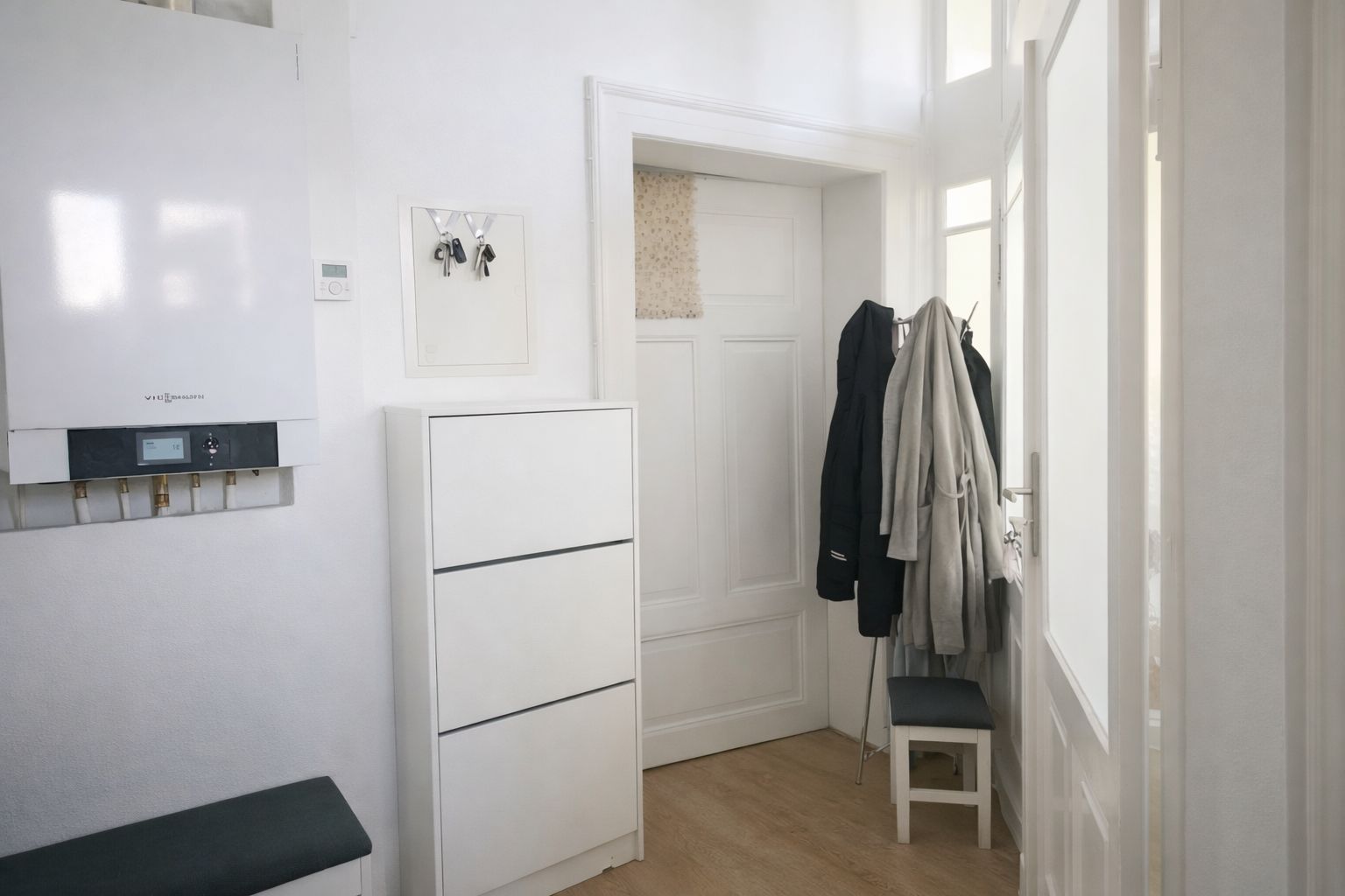 Helle Diele mit Schuhschrank, Garderobe, Stuhl und Gastherme an der Wand.