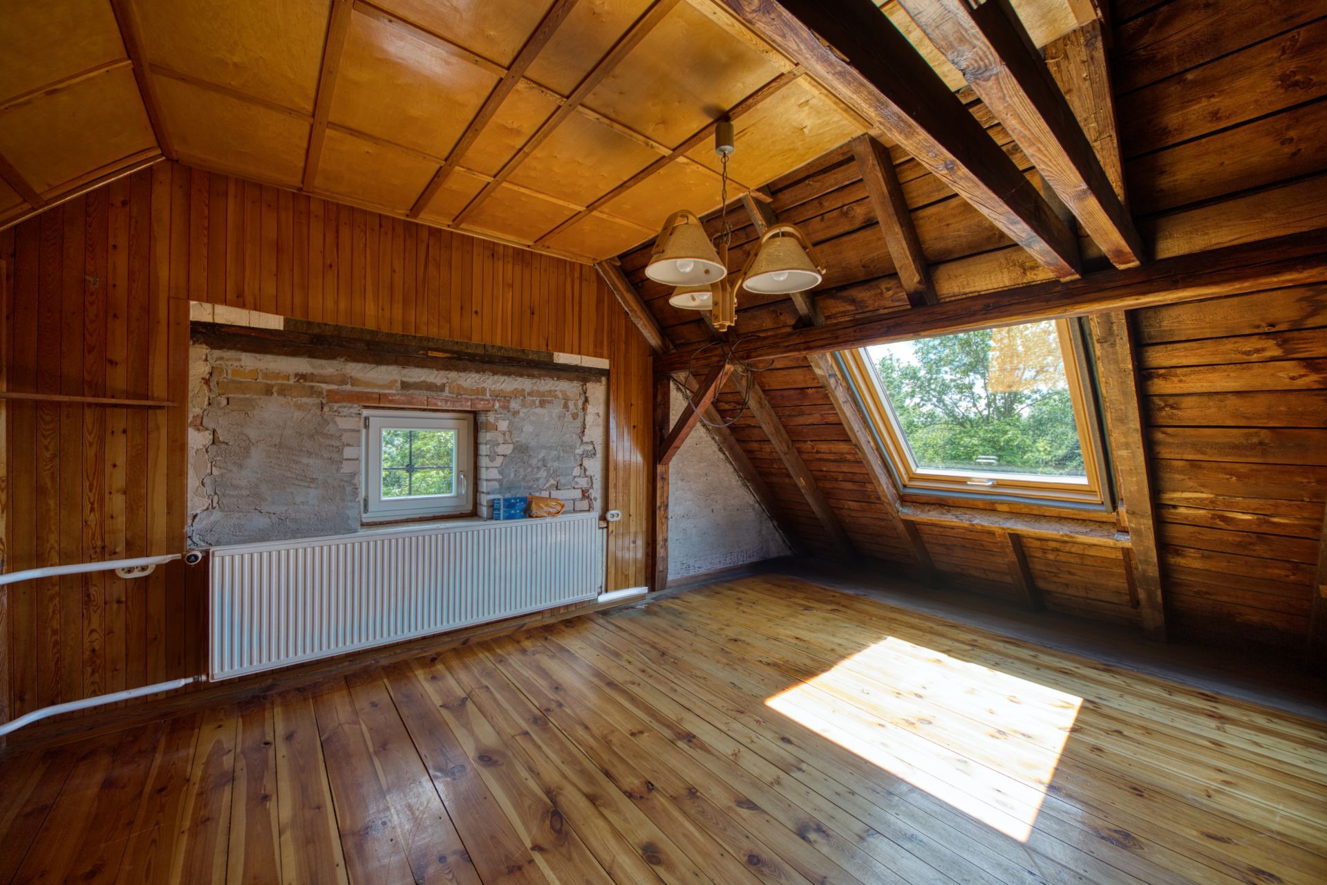 Dachzimmer mit Holzdecke, Holzfußboden, Fenster und Heizkörper, Sonnenlicht fällt herein.