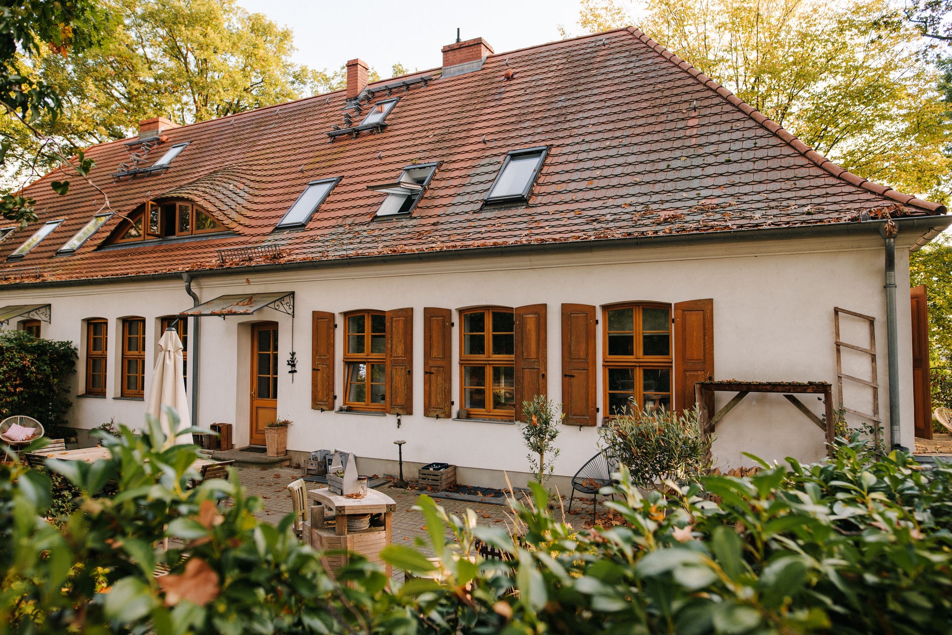 Zweistöckiges Wohnhaus mit roten Dachziegeln und braunen Fensterläden, umgeben von Garten.