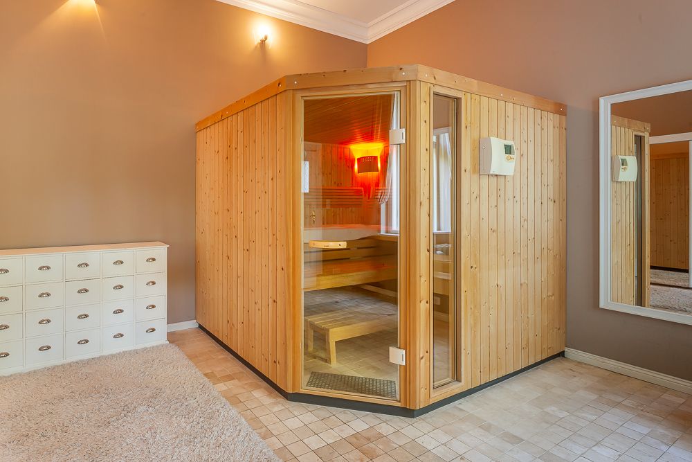 Helles Zimmer mit einer holzverkleideten Sauna, Spiegel und weißer Kommode.