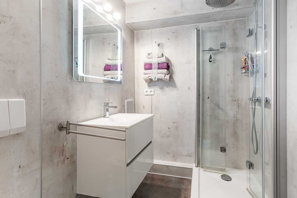 Modernes Badezimmer mit Spiegel, Waschbecken, Handtüchern und Dusche mit Glastür.