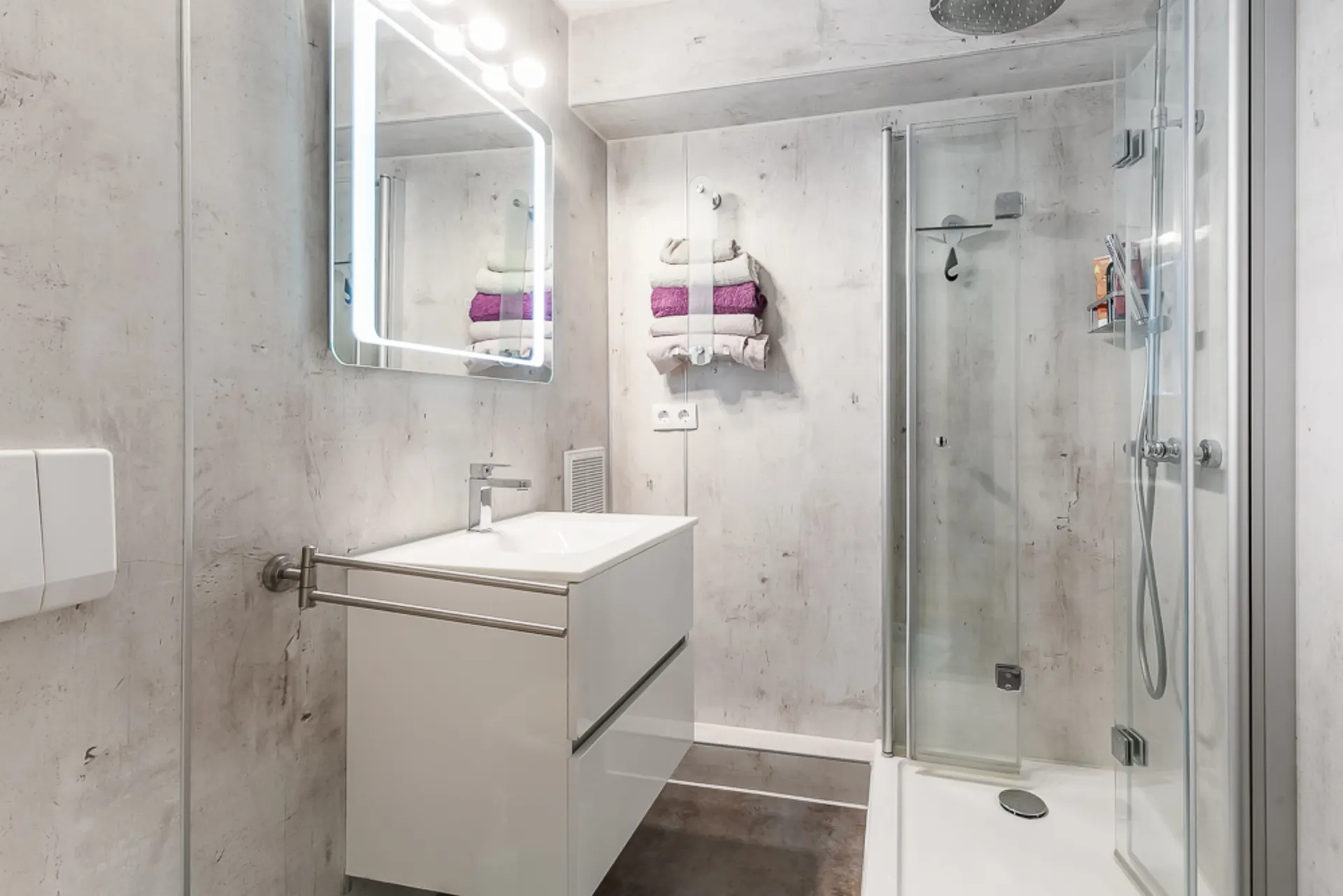 Modernes Badezimmer mit Spiegel, Waschbecken, Handtüchern und Dusche mit Glastür.