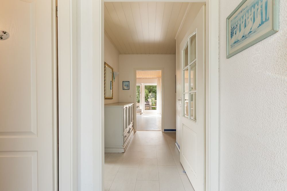 Heller Flur mit Kommode und Spiegel, Blick ins Wohnzimmer mit Gartenausgang.