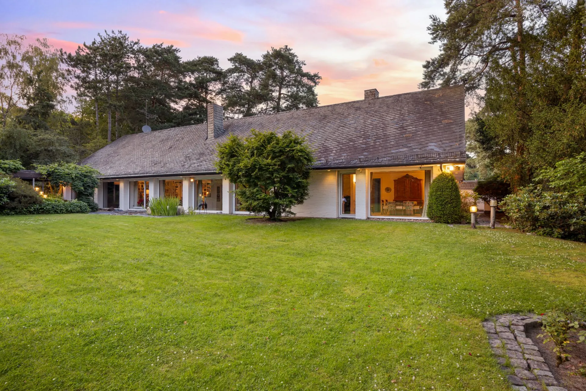 Einfamilienhaus mit großem Garten und Bäumen bei Sonnenuntergang.