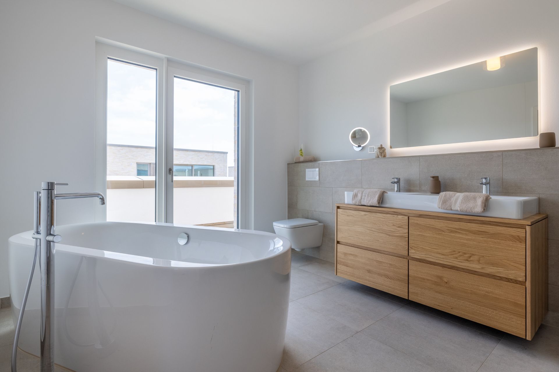 Modernes Badezimmer mit freistehender Badewanne, Doppelwaschbecken und großem beleuchtetem Spiegel.