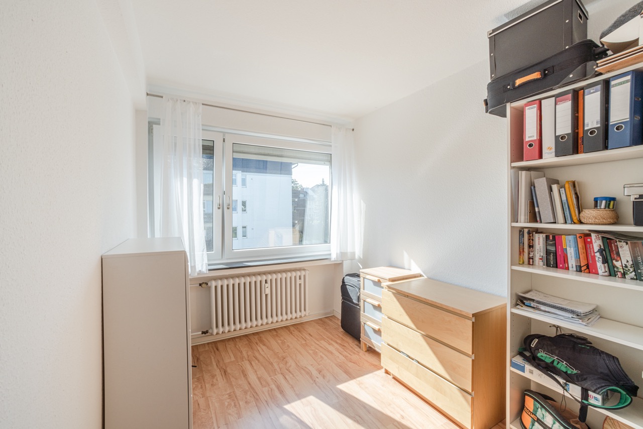 Helles Zimmer mit großem Fenster, Holzfußboden, Regal, Kommode und Aktenschrank.