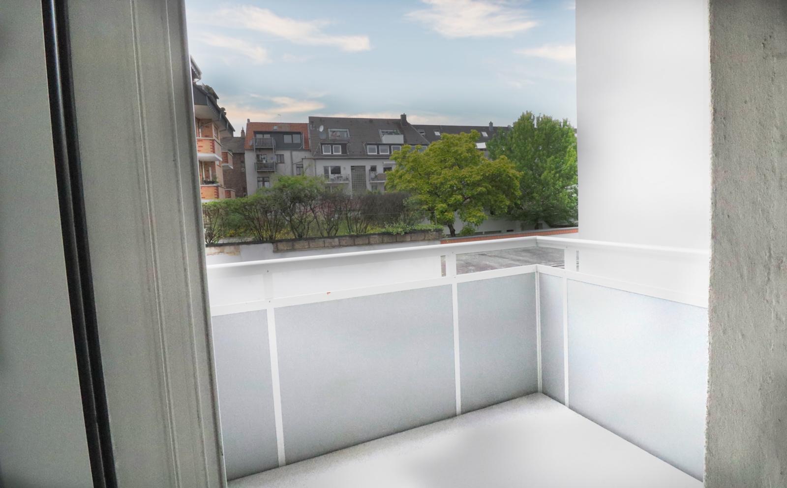 Kleiner Balkon mit weißem Geländer und Blick auf Bäume und Nachbarhäuser.