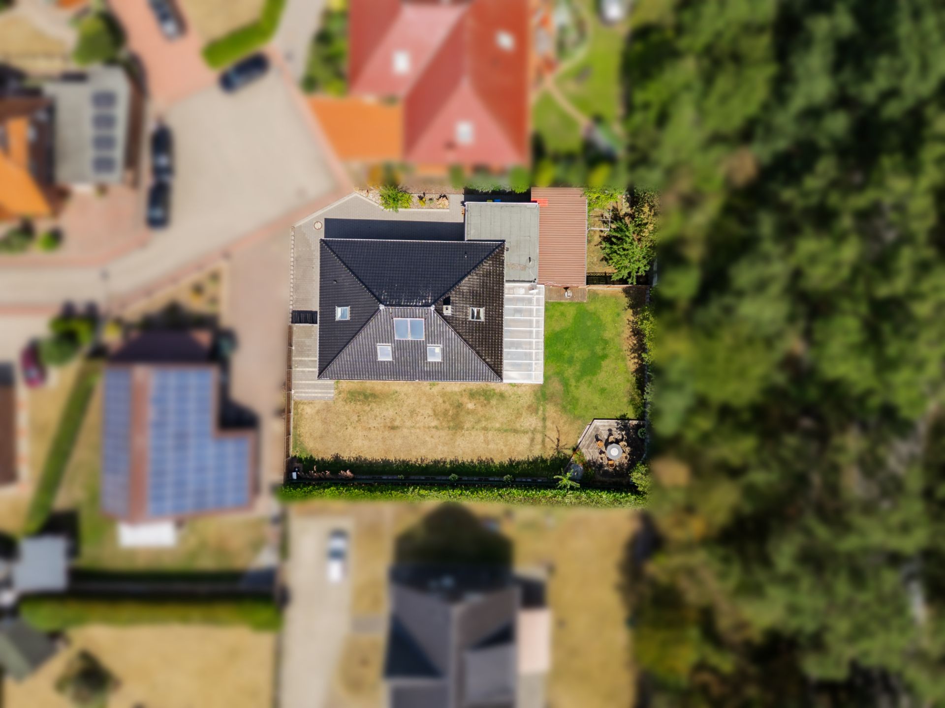 Luftaufnahme eines Einfamilienhauses mit Garten und Terrasse, umgeben von weiteren Häusern.