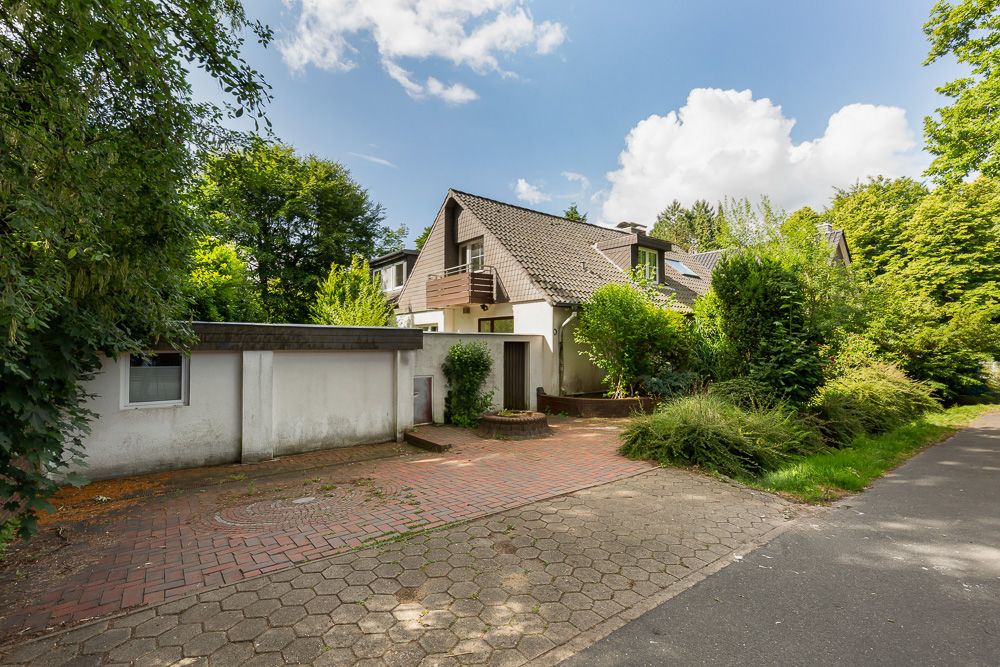 Einfamilienhaus mit Satteldach, Vorgarten und gepflasterter Einfahrt, umgeben von Bäumen.