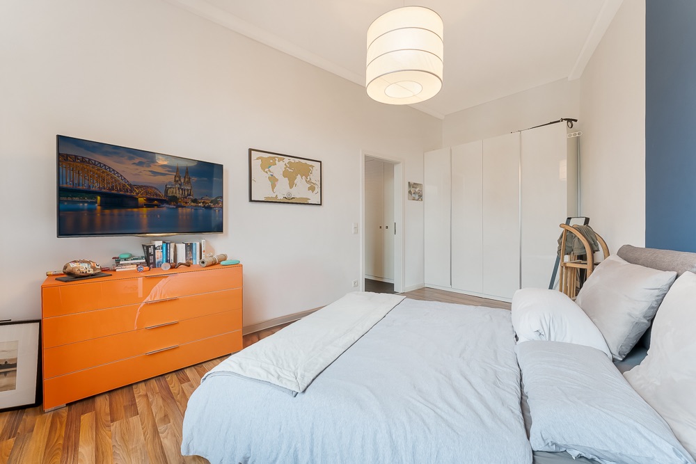Modernes Schlafzimmer mit Doppelbett, orangefarbener Kommode, Kleiderschrank und Wandbild.