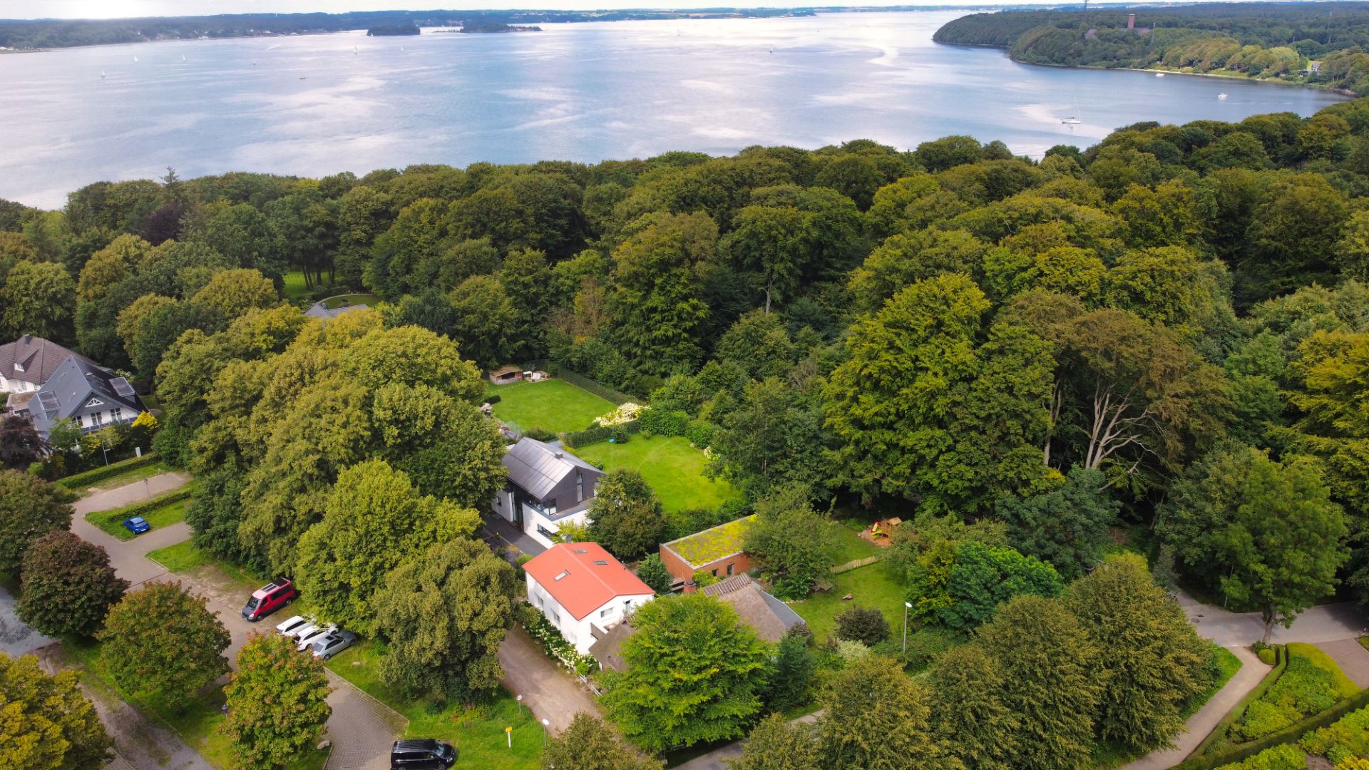 Luftaufnahme eines Hauses im Grünen nahe einem Wald und einem großen See.
