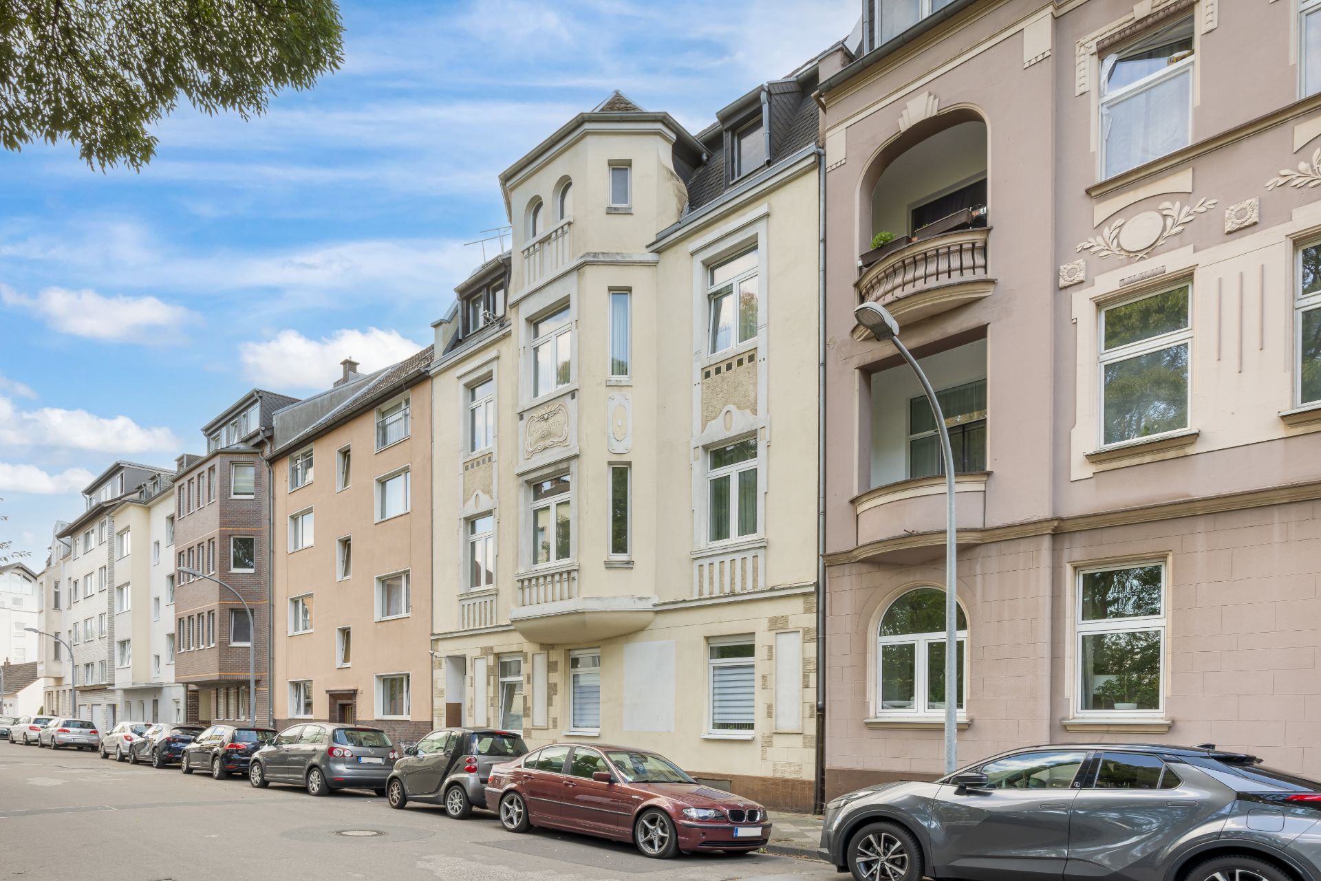 Mehrstöckige Wohnhäuser mit geparkten Autos entlang einer ruhigen Straße.