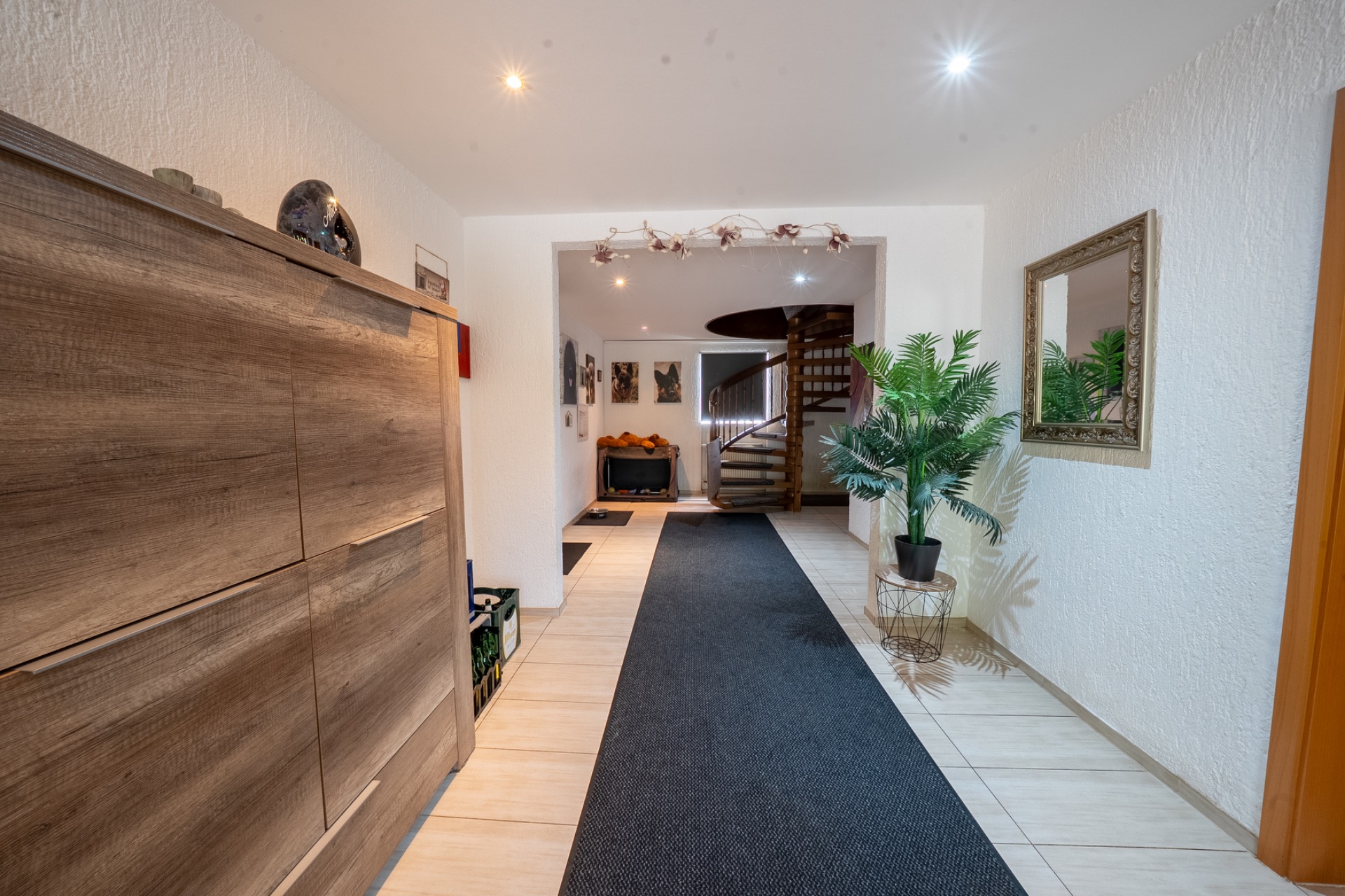 Heller Flur mit Holzschrank, Spiegel, Pflanze und Wendeltreppe im Hintergrund.