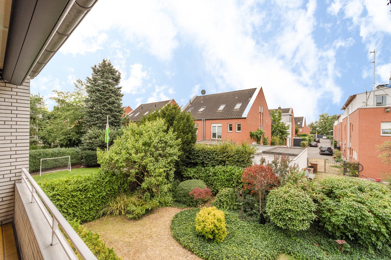 Blick vom Balkon auf einen grünen Garten mit Sträuchern und Fußballtor, Nachbarhäuser im Hintergrund.