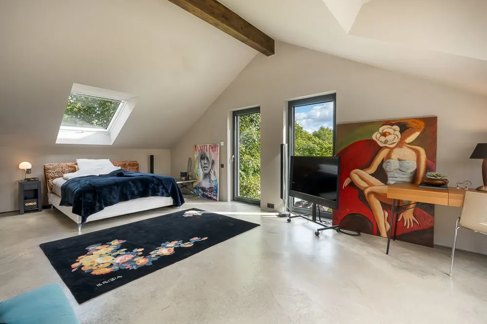 Modernes Schlafzimmer mit Dachfenster, Bett, Teppich, TV, Schreibtisch und großem Gemälde an der Wand.
