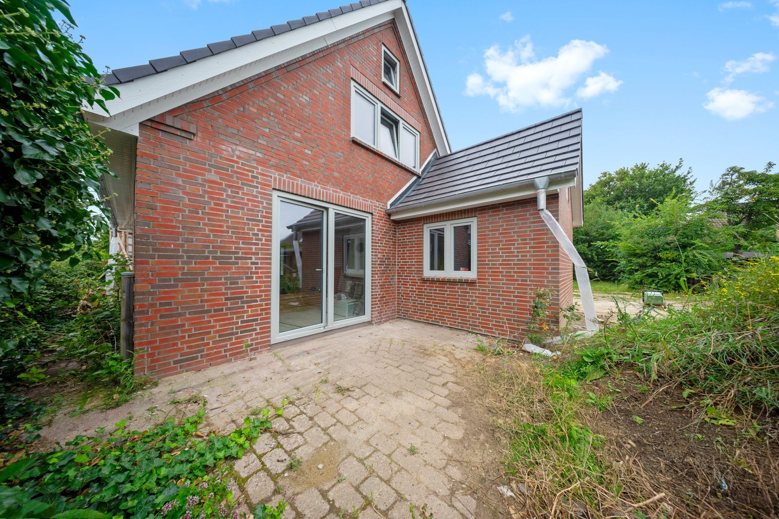 Backsteinwohnaus mit Schiebetür, Pflasterterrasse und Garten im Vordergrund.