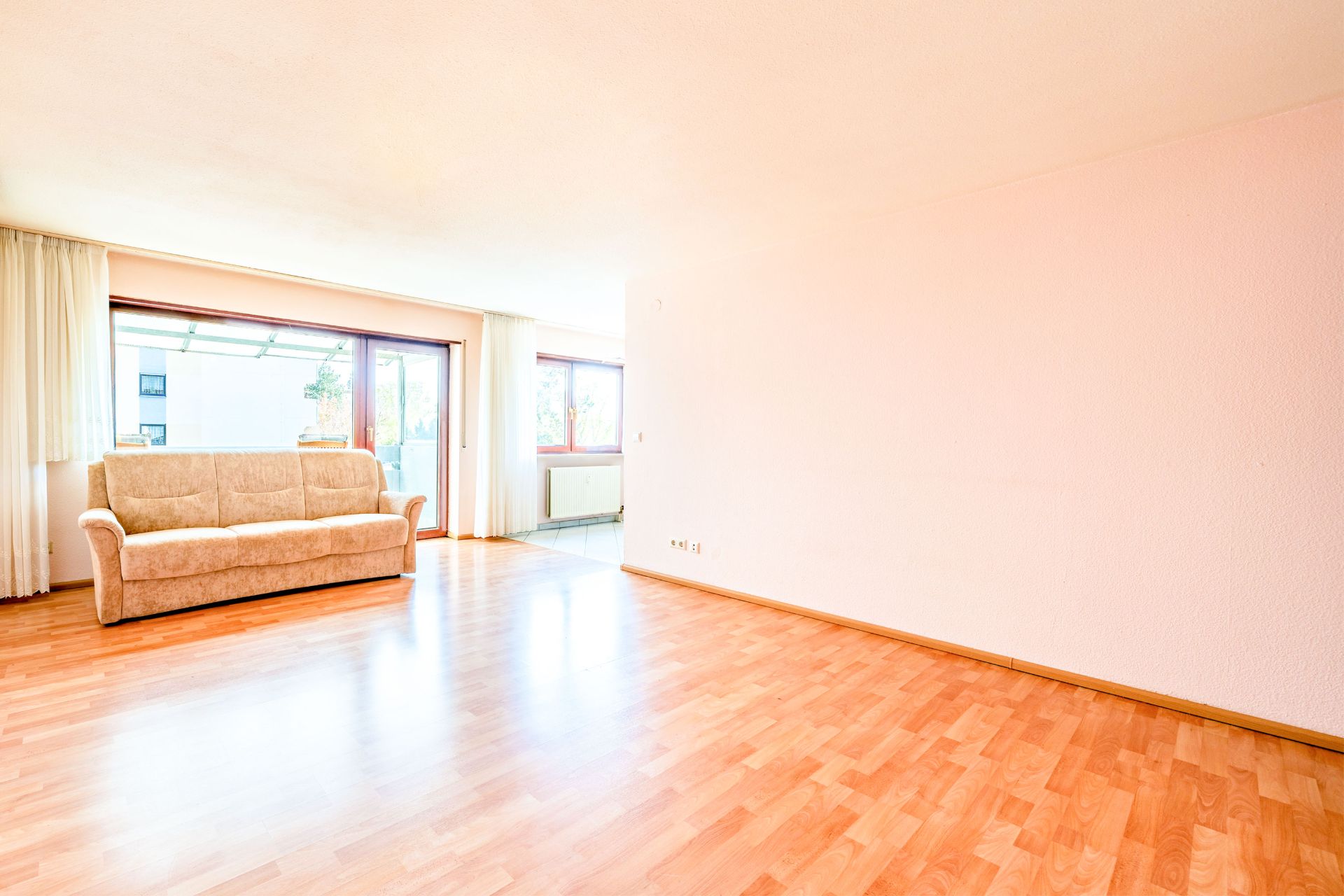Helles Wohnzimmer mit Parkettboden, beige Sofa und großen Fenstern.