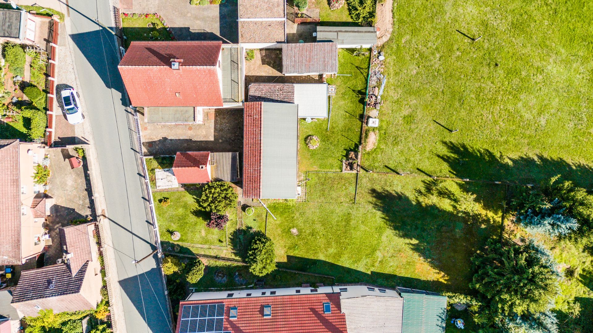 Luftbild von Wohnhäusern mit roten Dächern, Gärten und einer angrenzenden grünen Wiese.