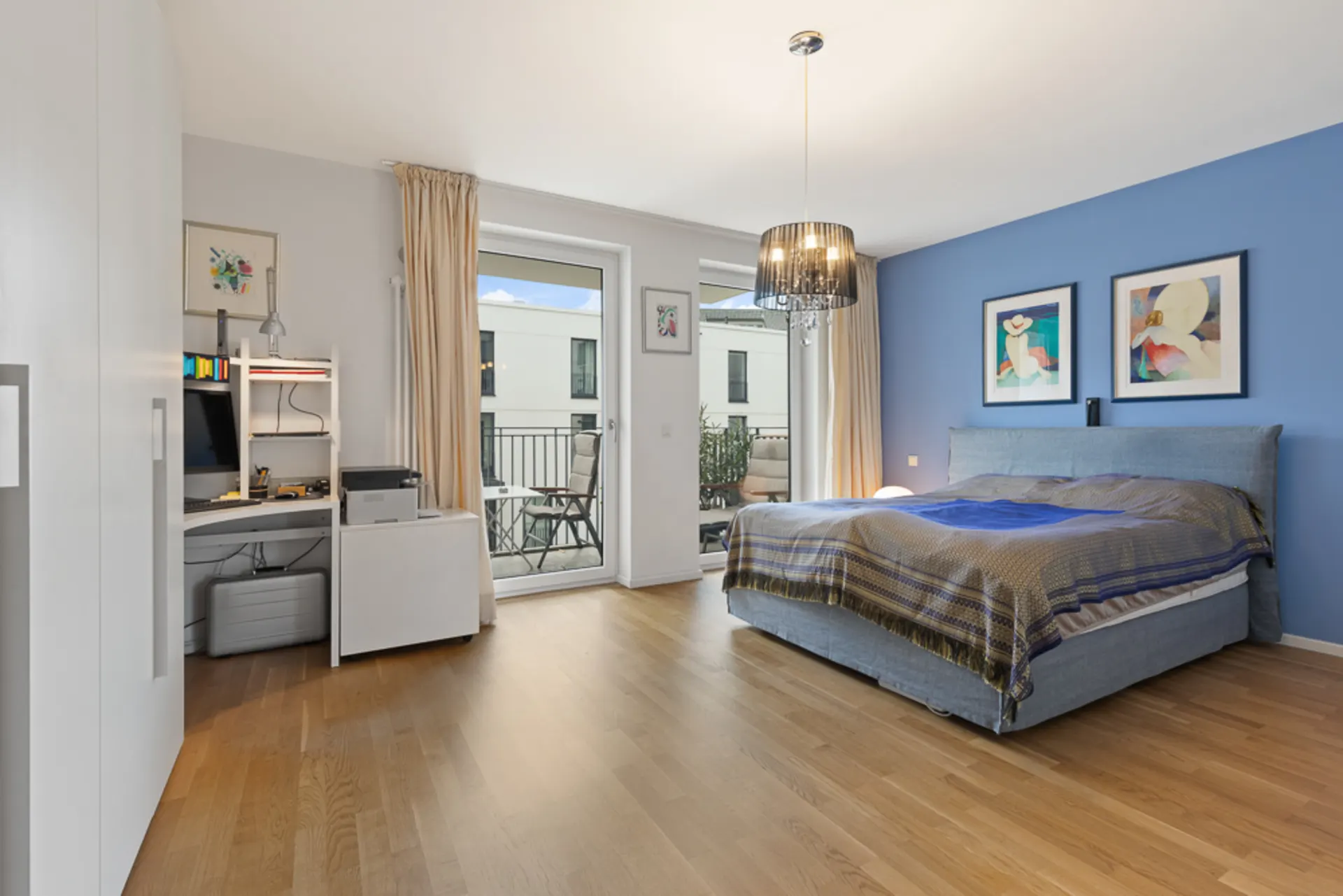 Modernes Schlafzimmer mit Schreibtisch, Doppelbett, Wandbildern und Balkonzugang.