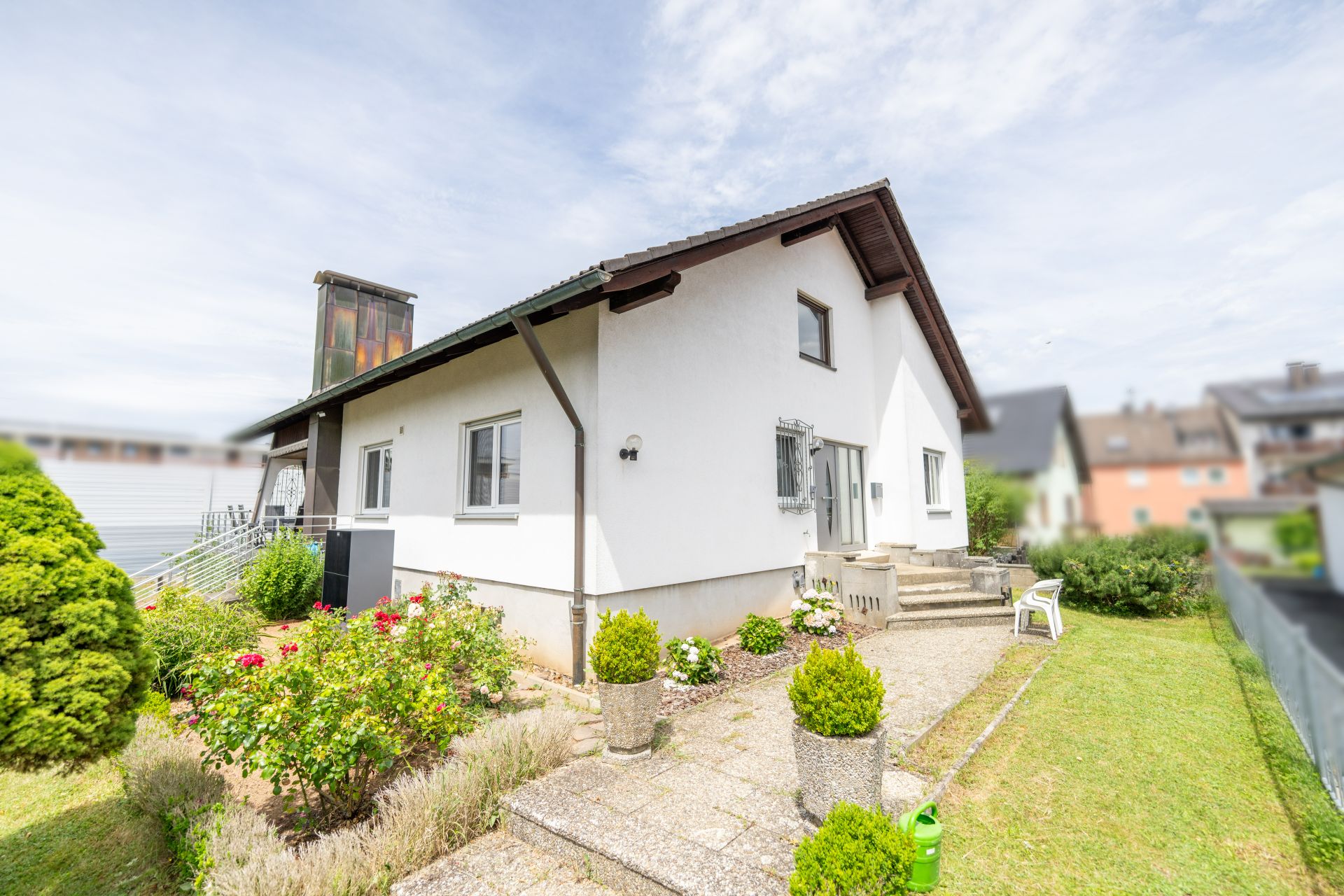 Weißes Einfamilienhaus mit kleinem Garten und mehreren Sträuchern, Außenbereich mit Sitzmöbeln.