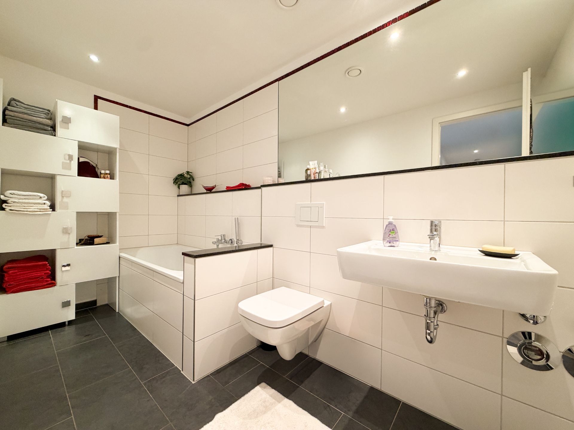 Modernes Badezimmer mit Badewanne, Waschbecken, WC und Regal mit Handtüchern.