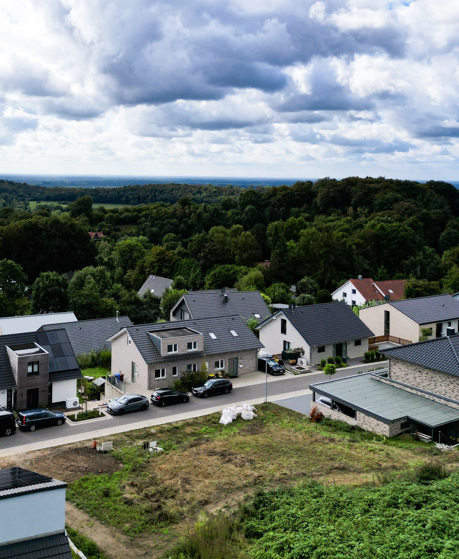Wohnsiedlung mit Einfamilienhäusern, Autos vor den Häusern und viel Grün im Hintergrund.
