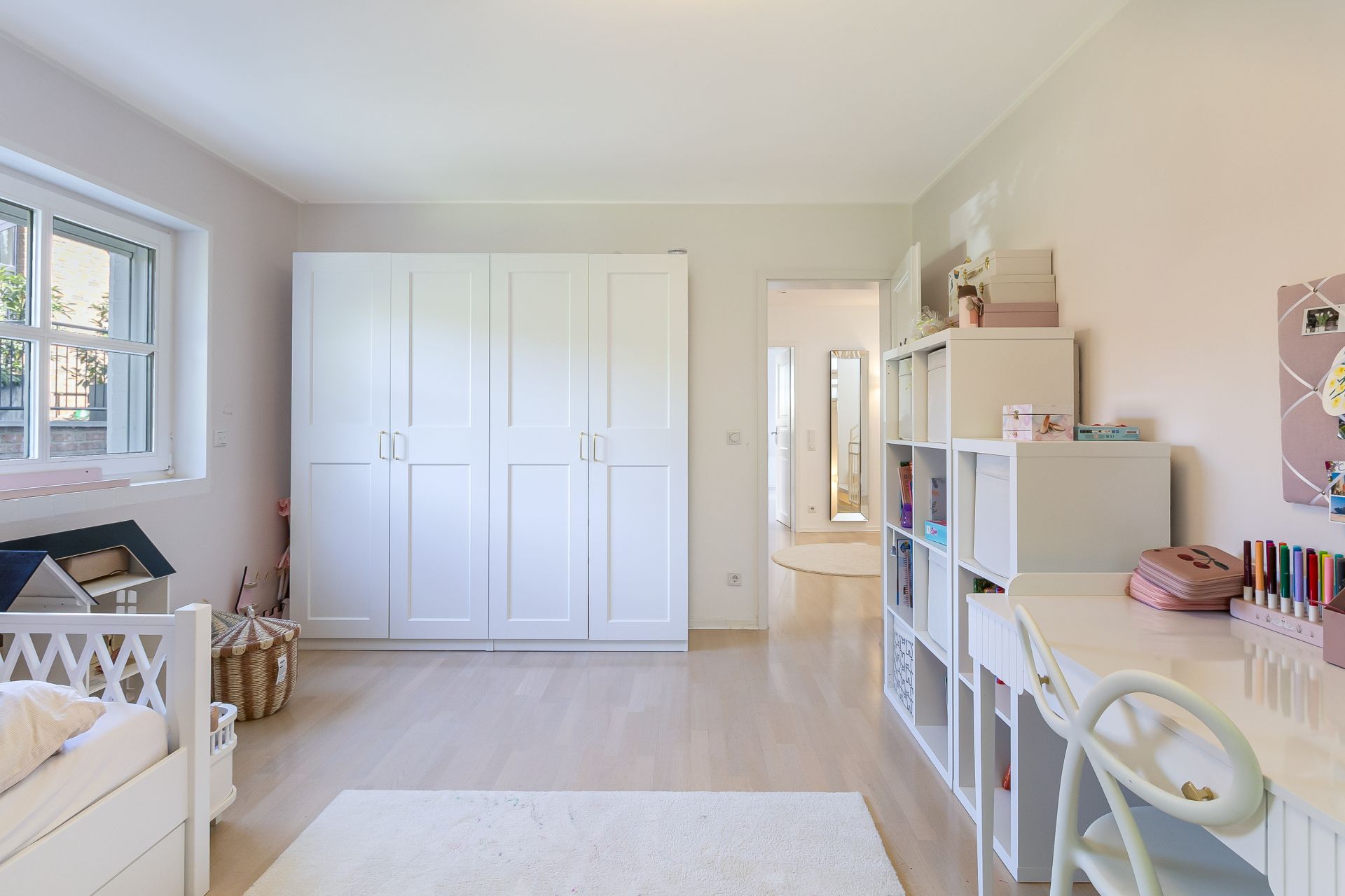 Helles Kinderzimmer mit Schreibtisch, Regalen, Bett und großem weißen Kleiderschrank.