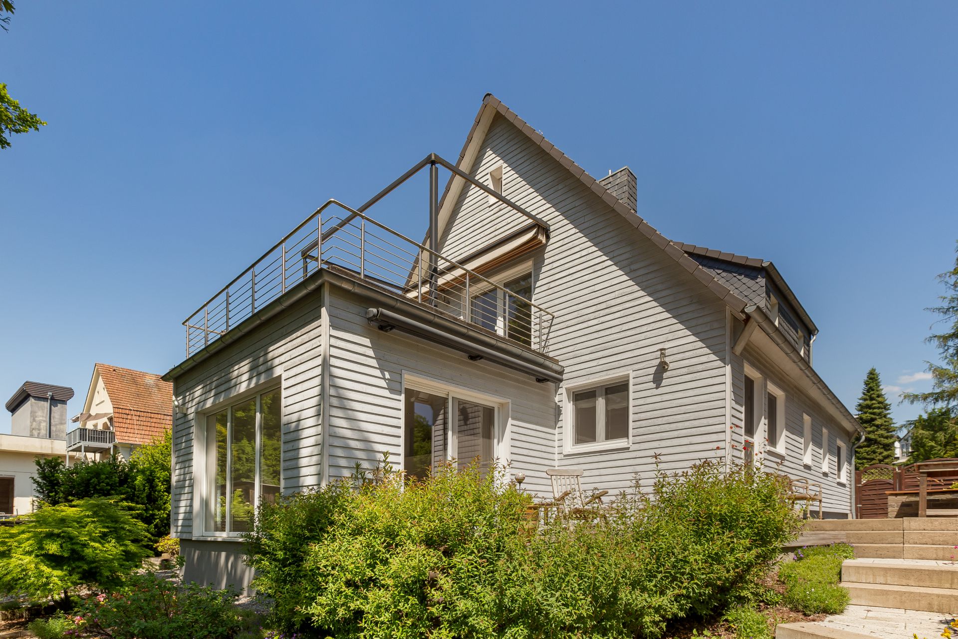 Modernes Wohnhaus mit großer Fensterfront, Balkon und Garten unter blauem Himmel.
