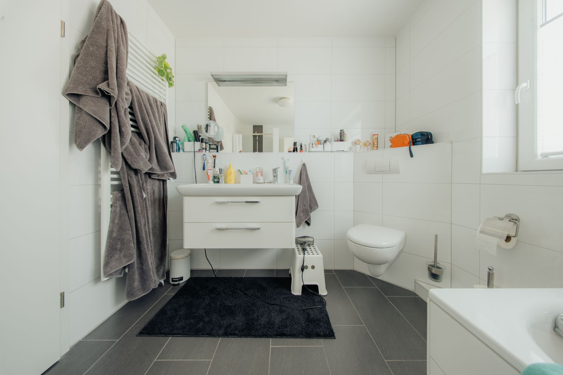 Modernes Badezimmer mit Waschbecken, Spiegel, WC und Badewanne, diverse Pflegeprodukte auf den Ablagen.