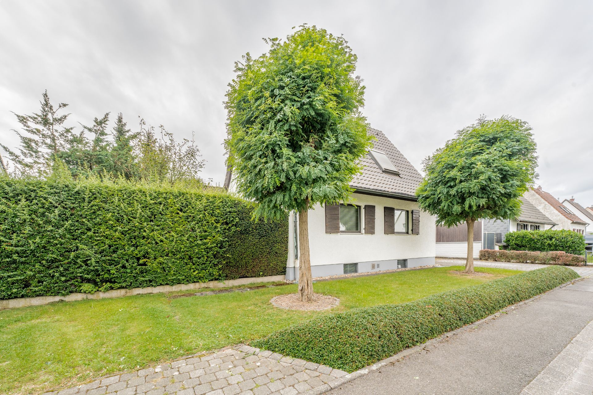 Vorderansicht eines Einfamilienhauses mit Vorgarten, Gehweg und mehreren Bäumen.