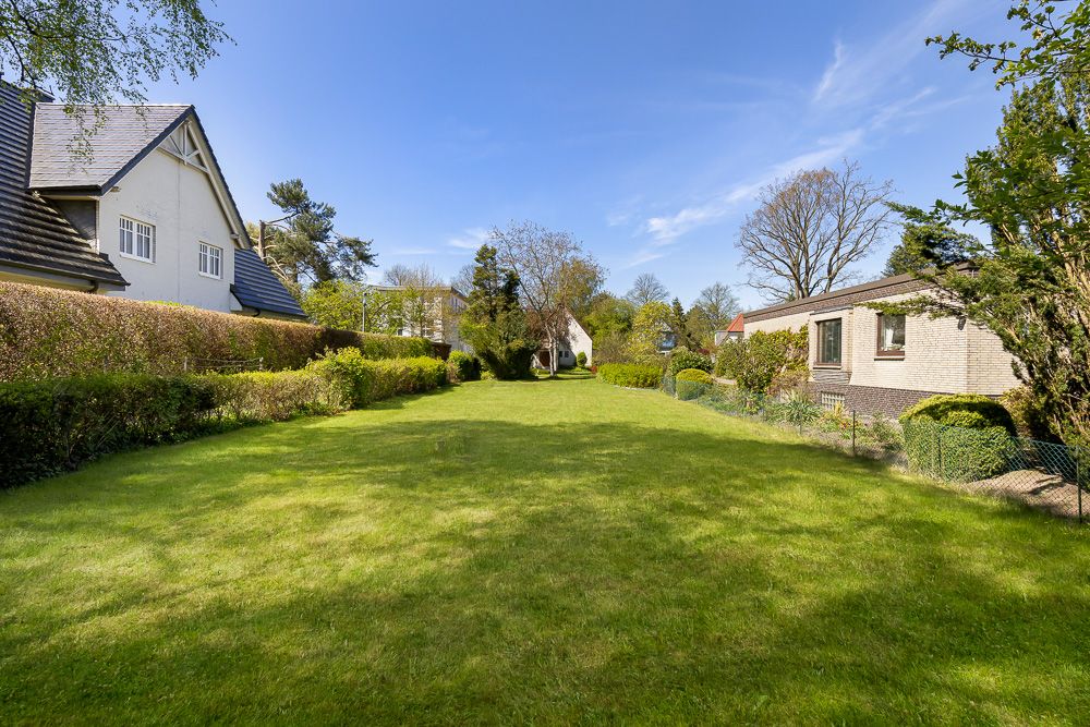 Großer Garten mit Rasenfläche, Büschen und zwei Häusern an den Seiten.