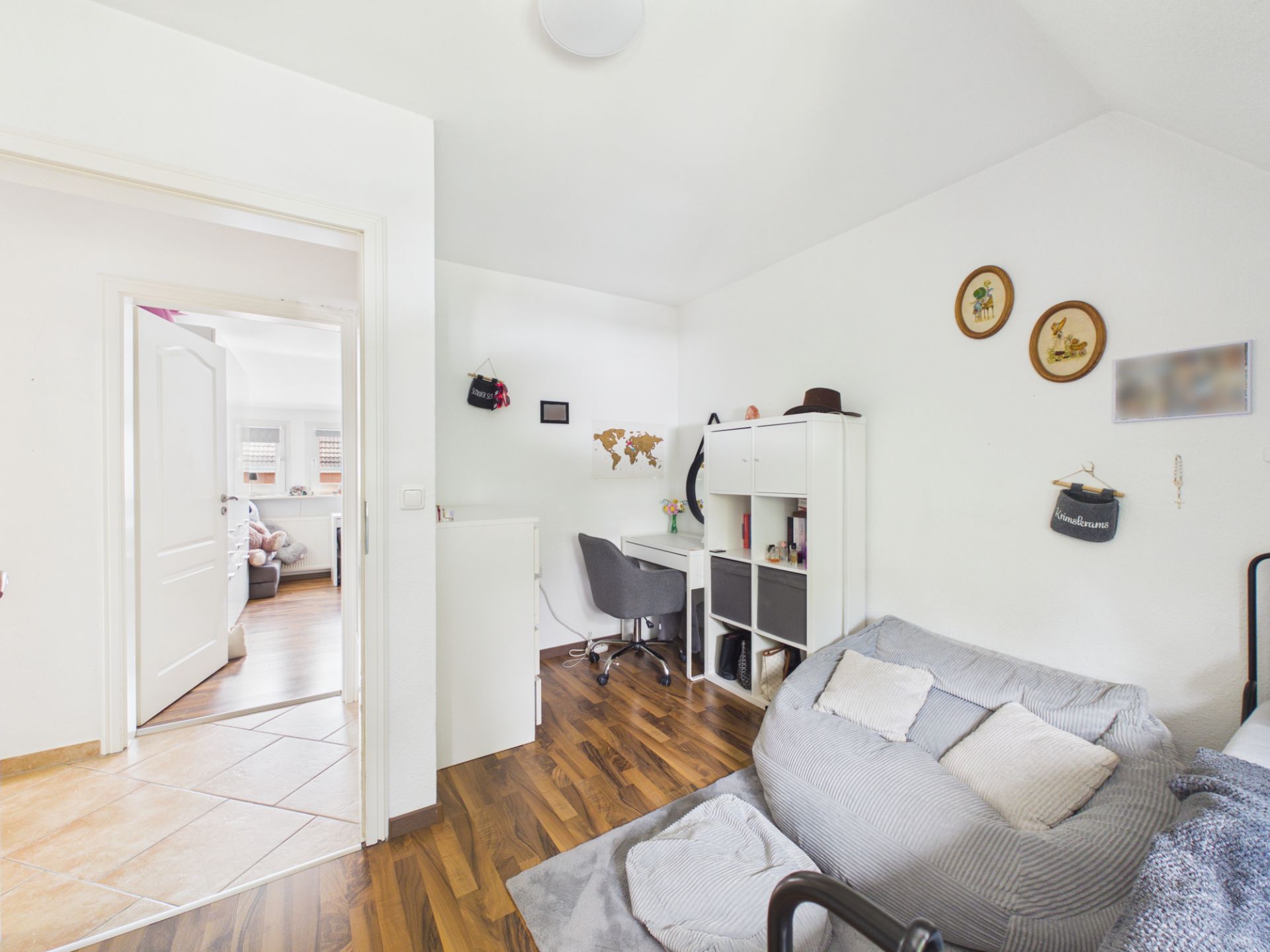 Helles Wohn- oder Arbeitszimmer mit Schreibtisch, Regal, Sessel und Holzboden.