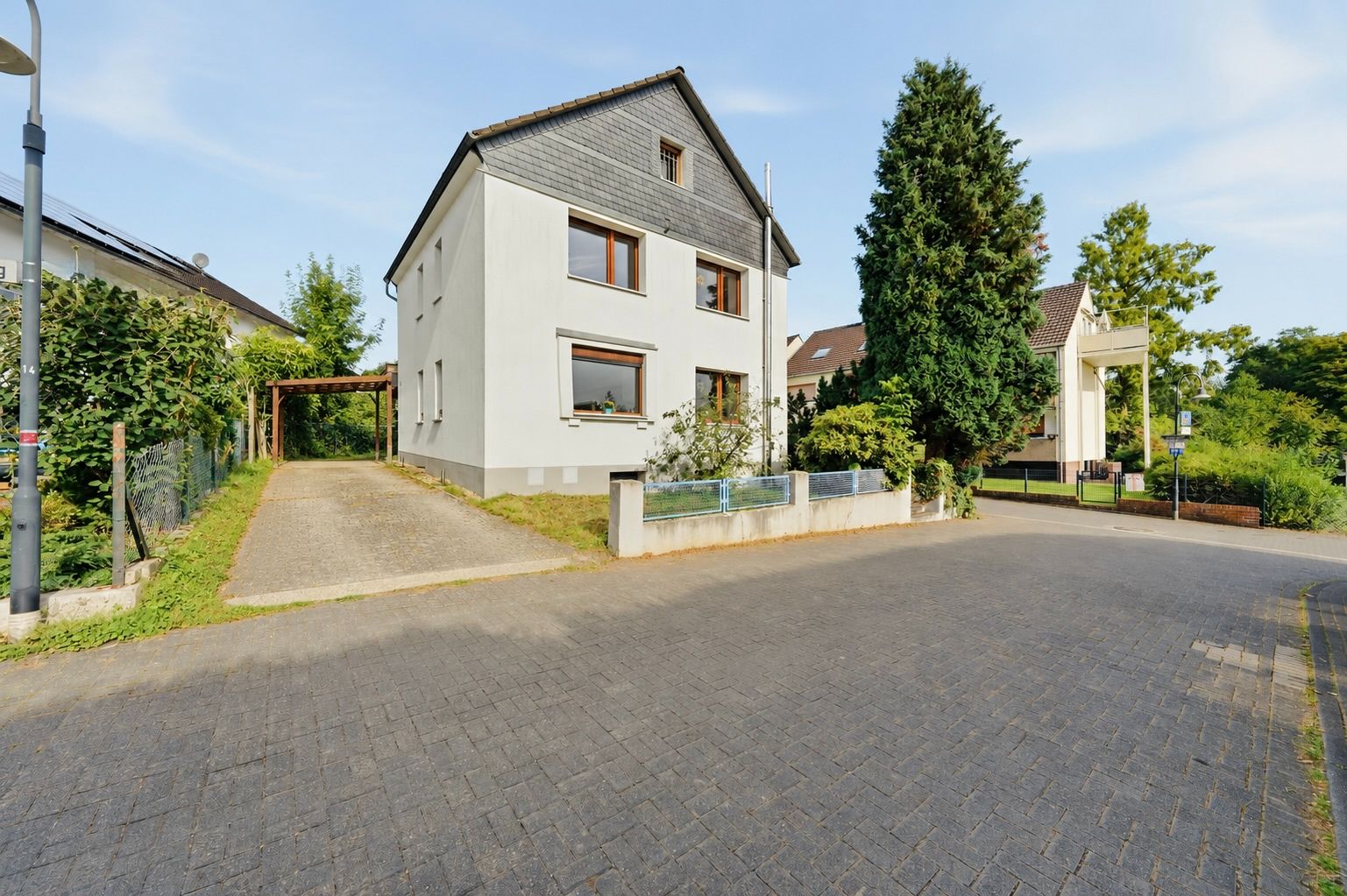 Zweistöckiges Wohnhaus mit Garten, Einfahrt und Bäumen an einer ruhigen Straße.