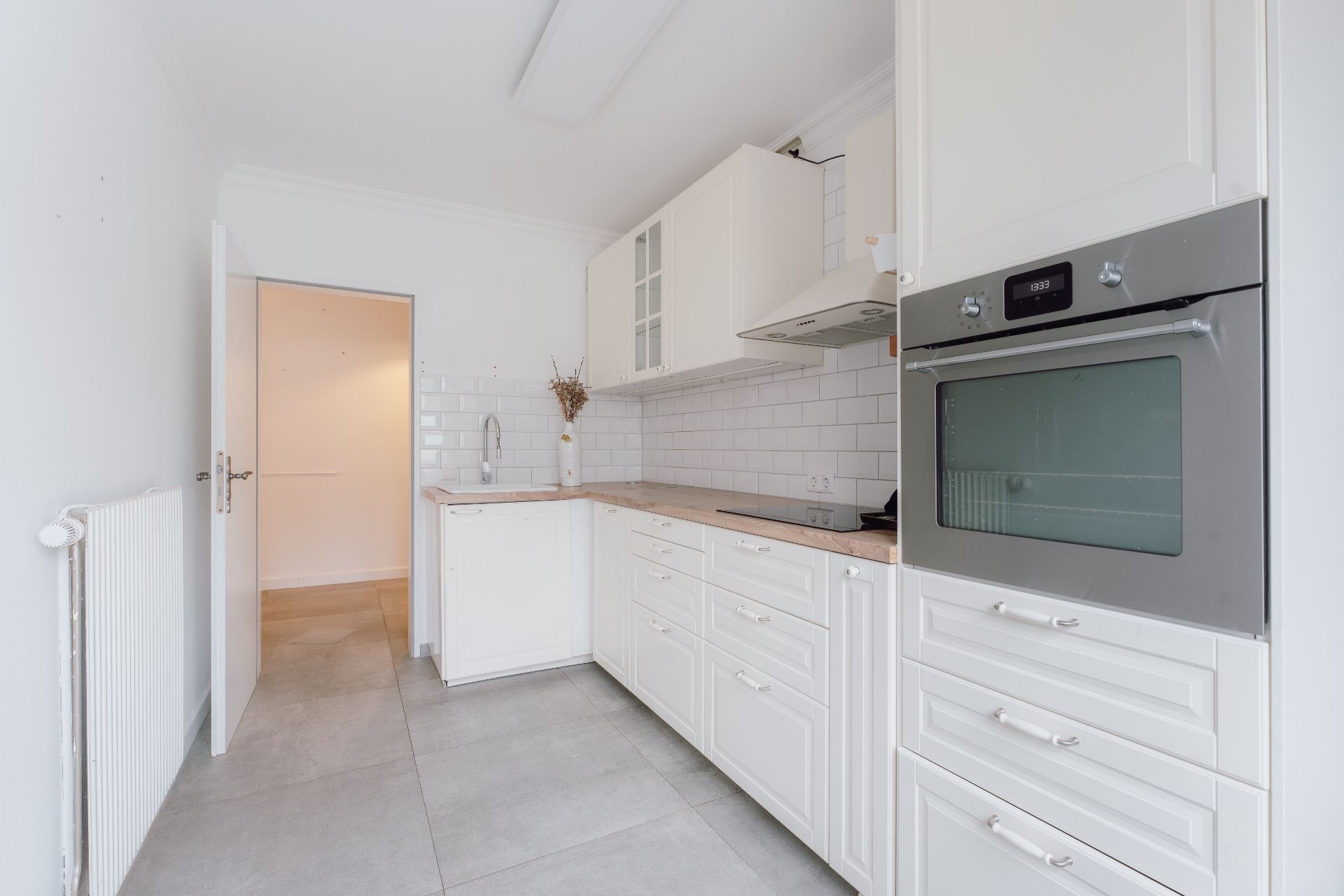 Helle Einbauküche mit weißen Schränken, Backofen und Keramikspüle.
