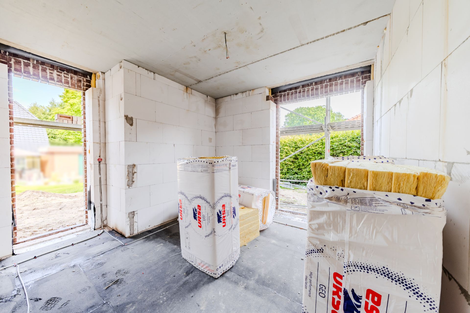 Rohbauzimmer mit Baumaterialien und großen Fensteraussparungen.