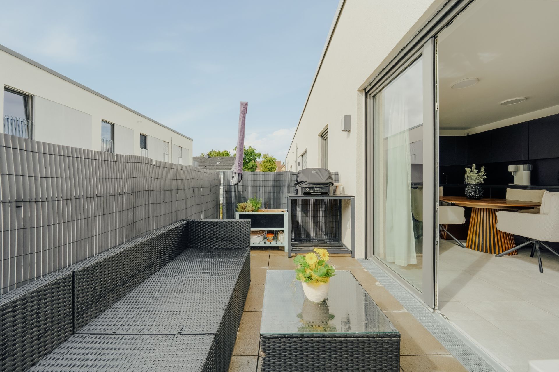 Moderne Terrasse mit Sitzgruppe, Tisch, Grill und Zugang zum Essbereich durch eine Glasschiebetür.