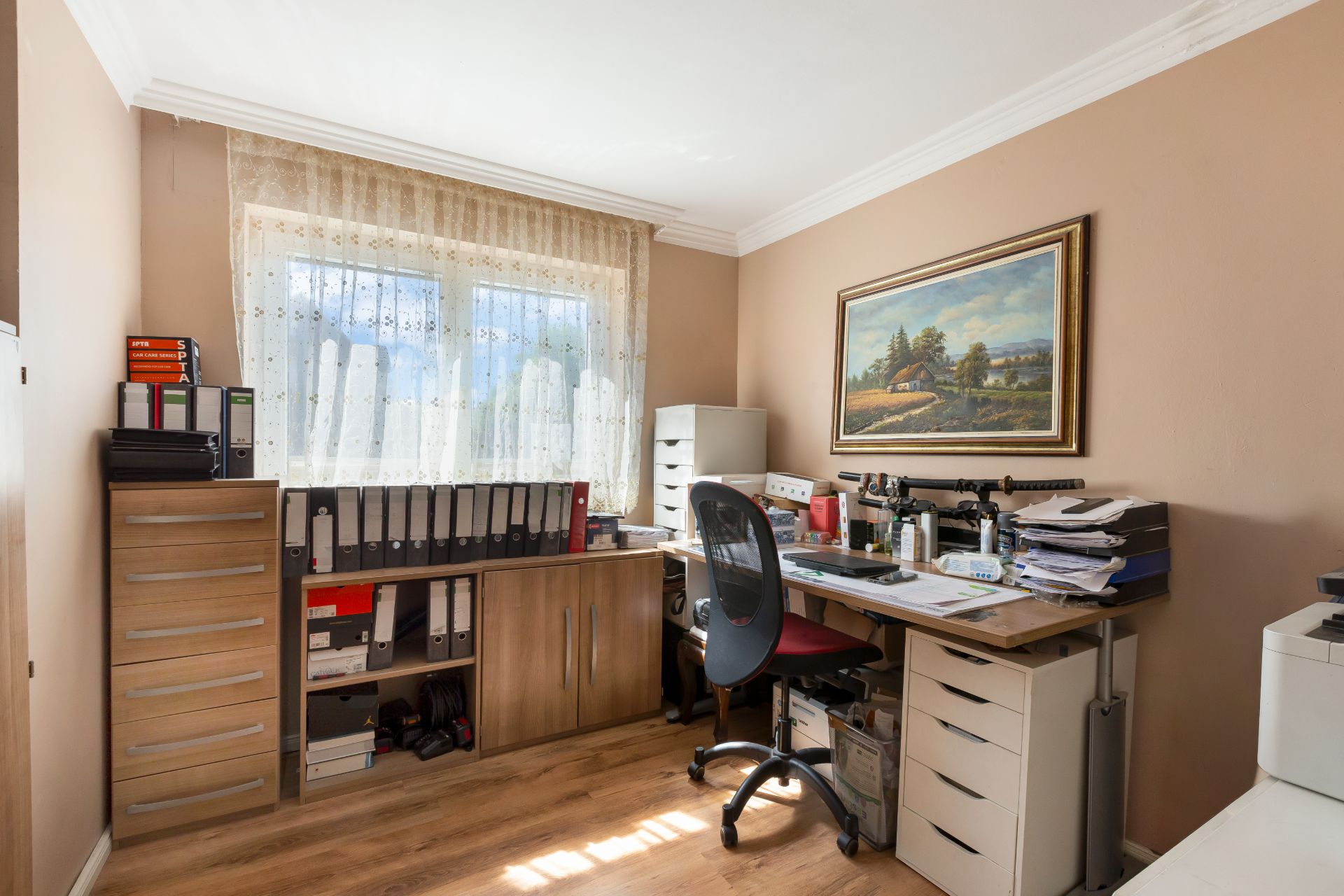 Helles Arbeitszimmer mit Schreibtisch, Bürostuhl, Regalen und großem Fenster.