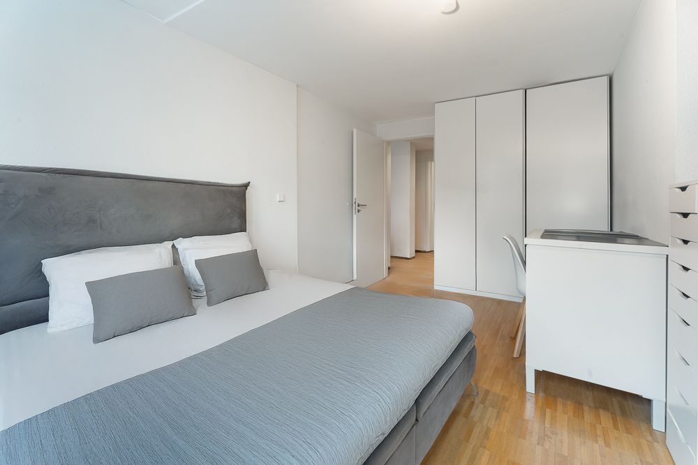 Modernes Schlafzimmer mit Doppelbett, Schreibtisch, Stuhl und weißem Kleiderschrank auf Holzboden.