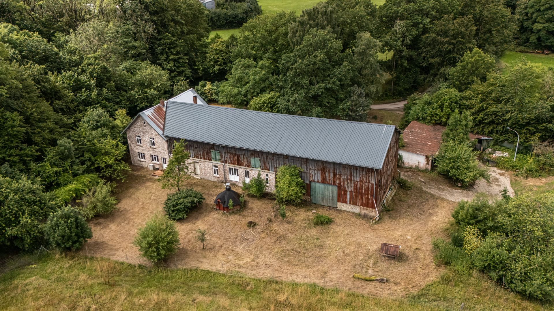 Langes, einstöckiges Gebäude mit Wellblechdach, umgeben von Bäumen und Grasfläche.