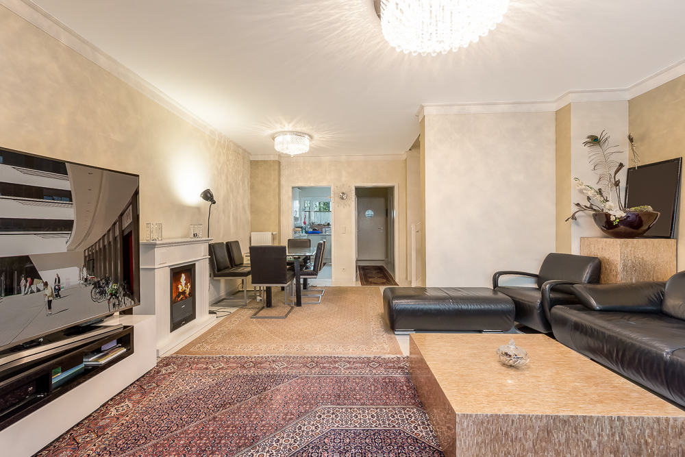 Helles Wohnzimmer mit schwarzem Ledersofa, Fernseher, Kamin und Esstisch mit Stühlen.