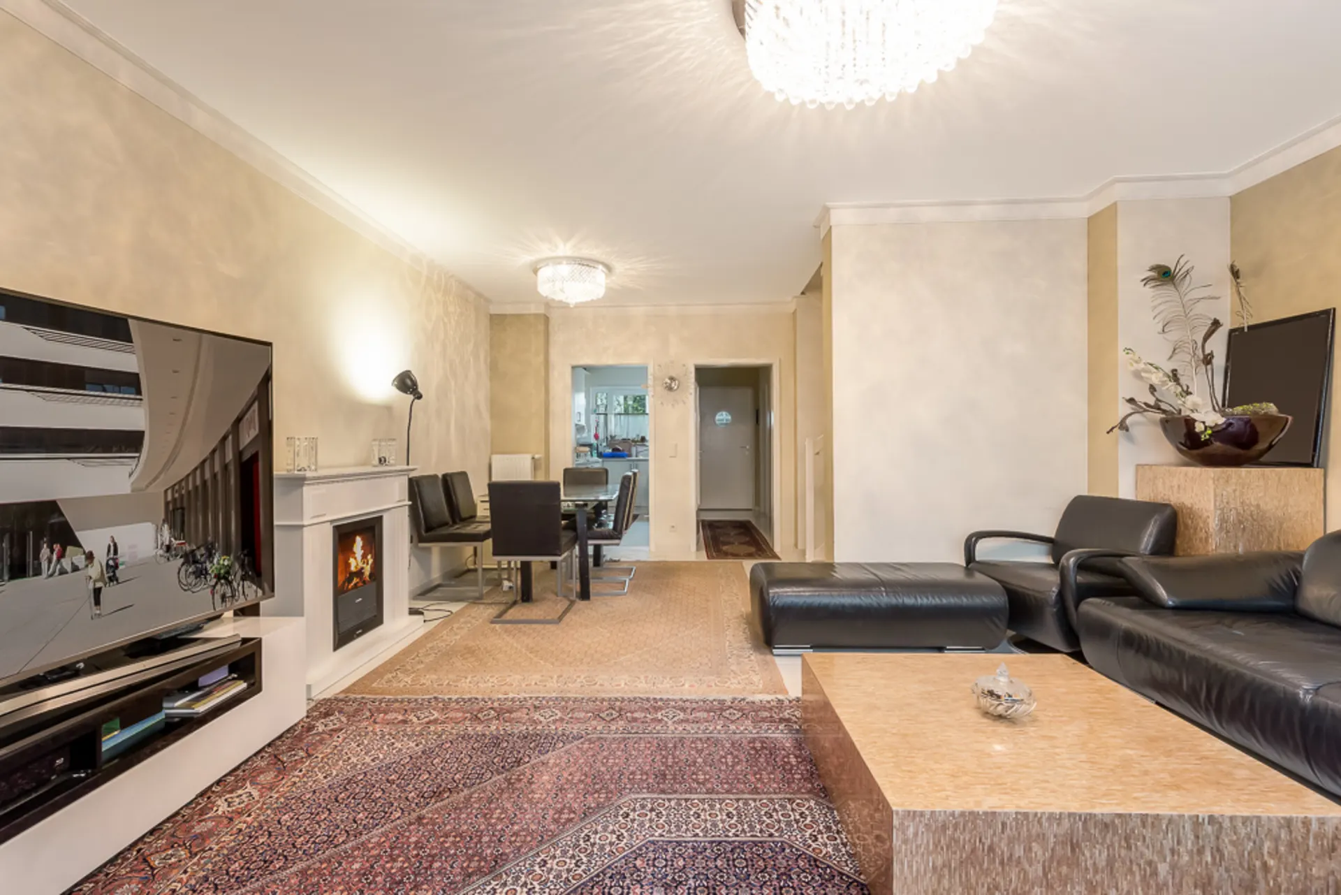 Helles Wohnzimmer mit schwarzem Ledersofa, Fernseher, Kamin und Esstisch mit Stühlen.