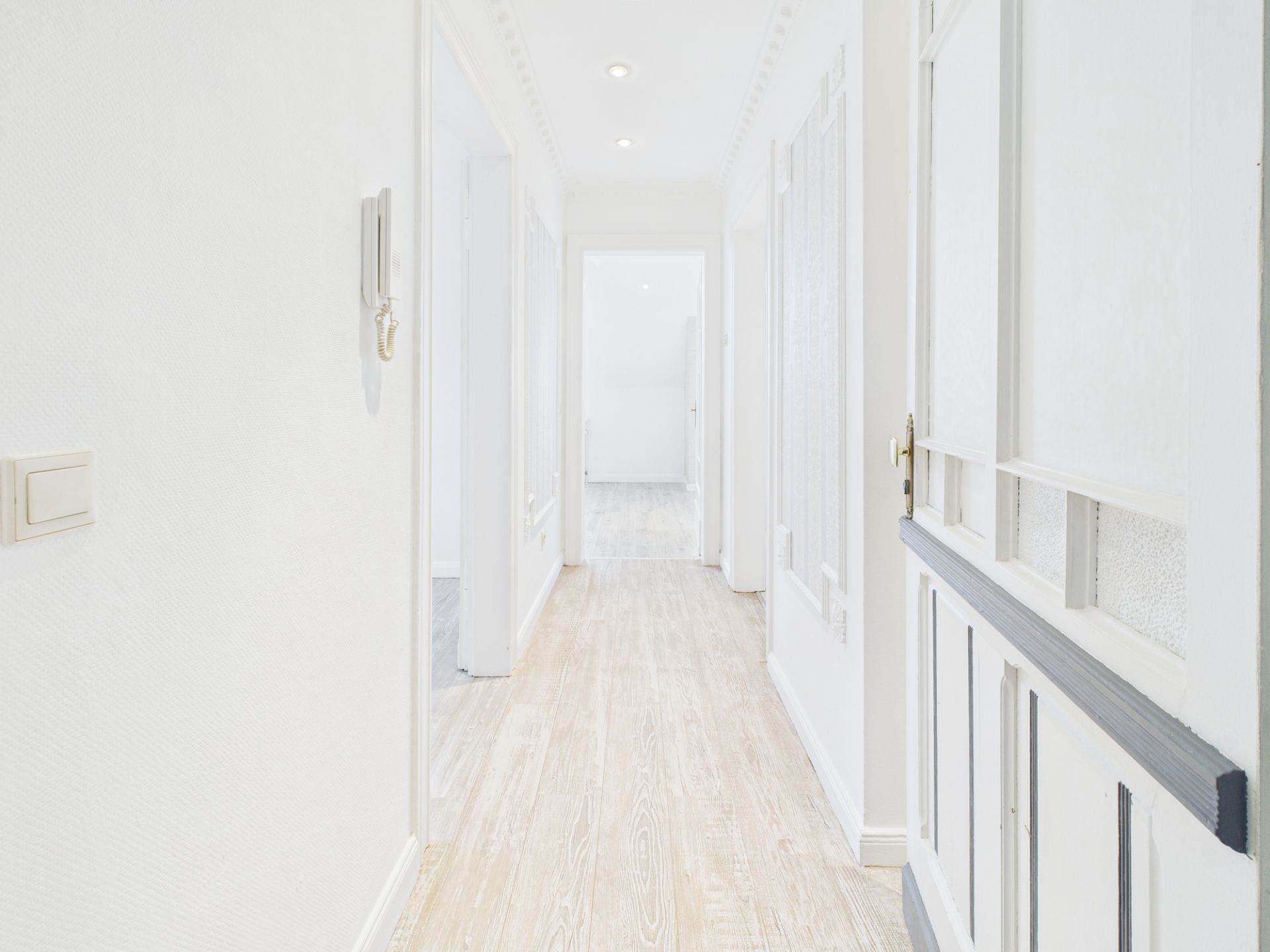 Heller Flur mit Holzboden, weißen Wänden und mehreren Türen in einem Wohnhaus.