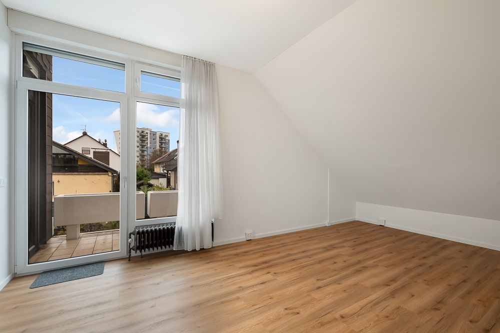 Helles Zimmer mit Holzfußboden, großen Fenstern und Zugang zu einem Balkon.